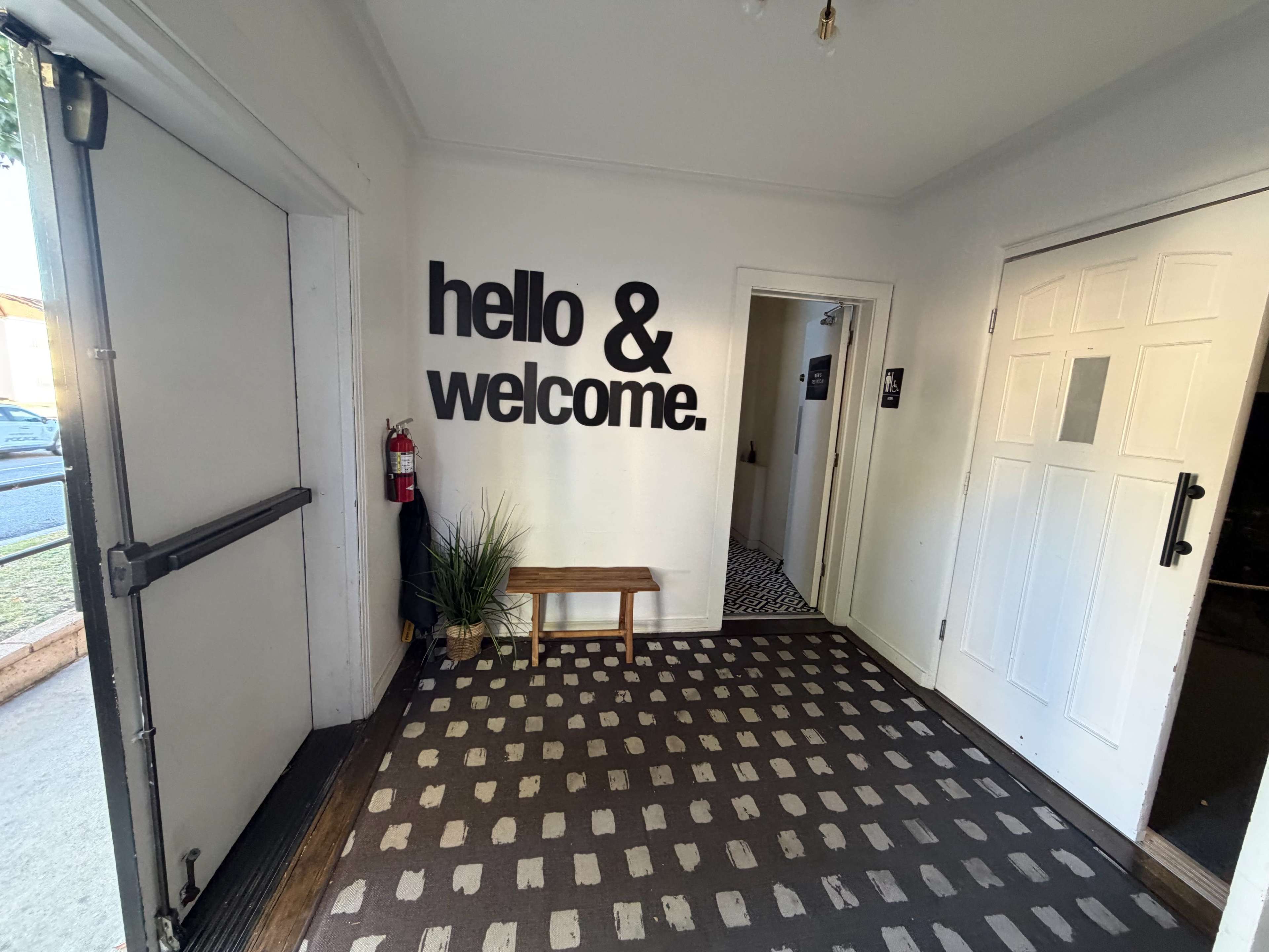 The image shows an entryway with a wall displaying the words "hello & welcome," a bench, and a patterned floor.