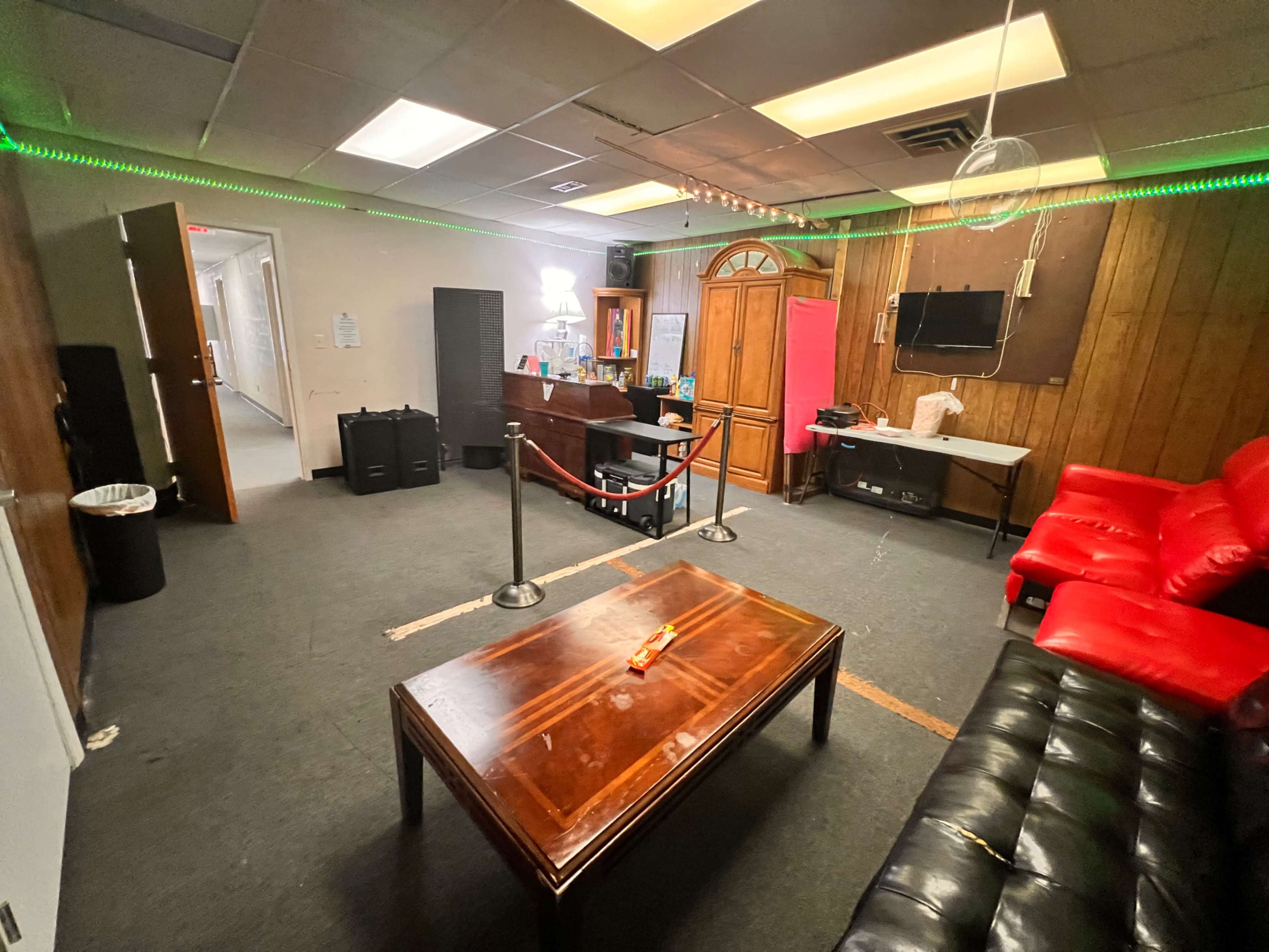 An indoor lounge area with red and black couches, a wooden coffee table, and a reception desk in the background.