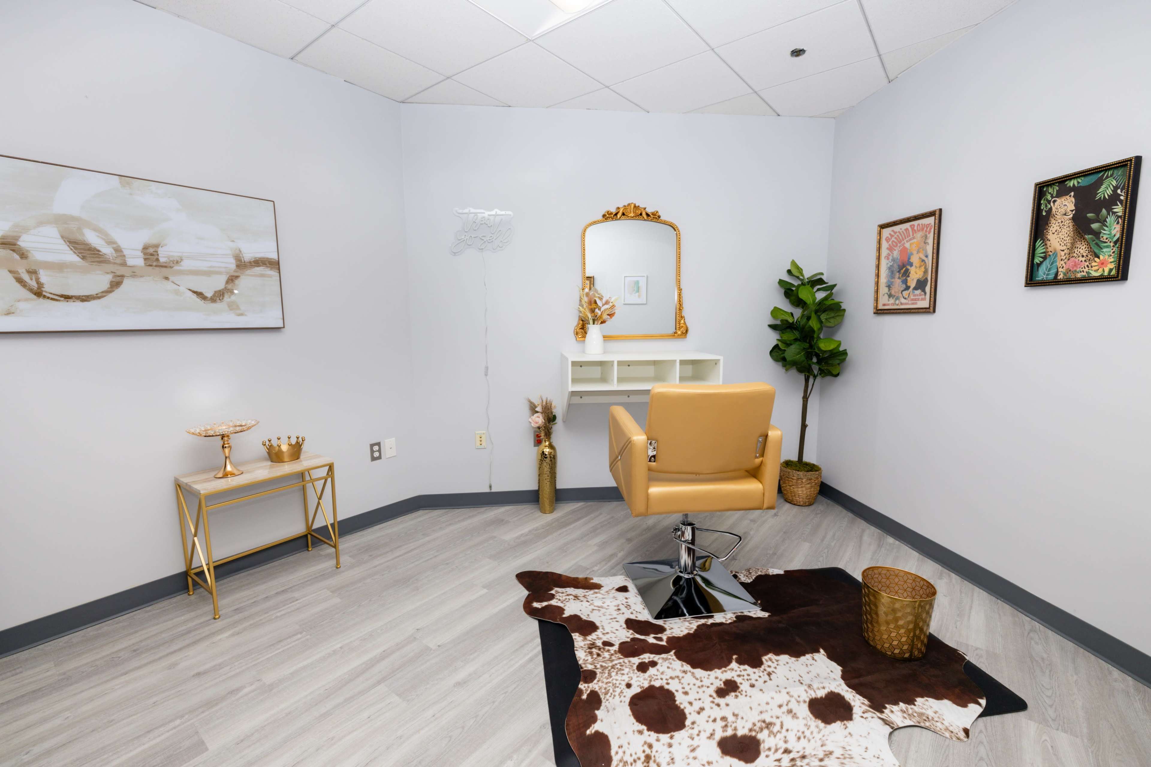 The image shows a minimalist salon room featuring a yellow styling chair, a wall-mounted mirror, and decorative art pieces.