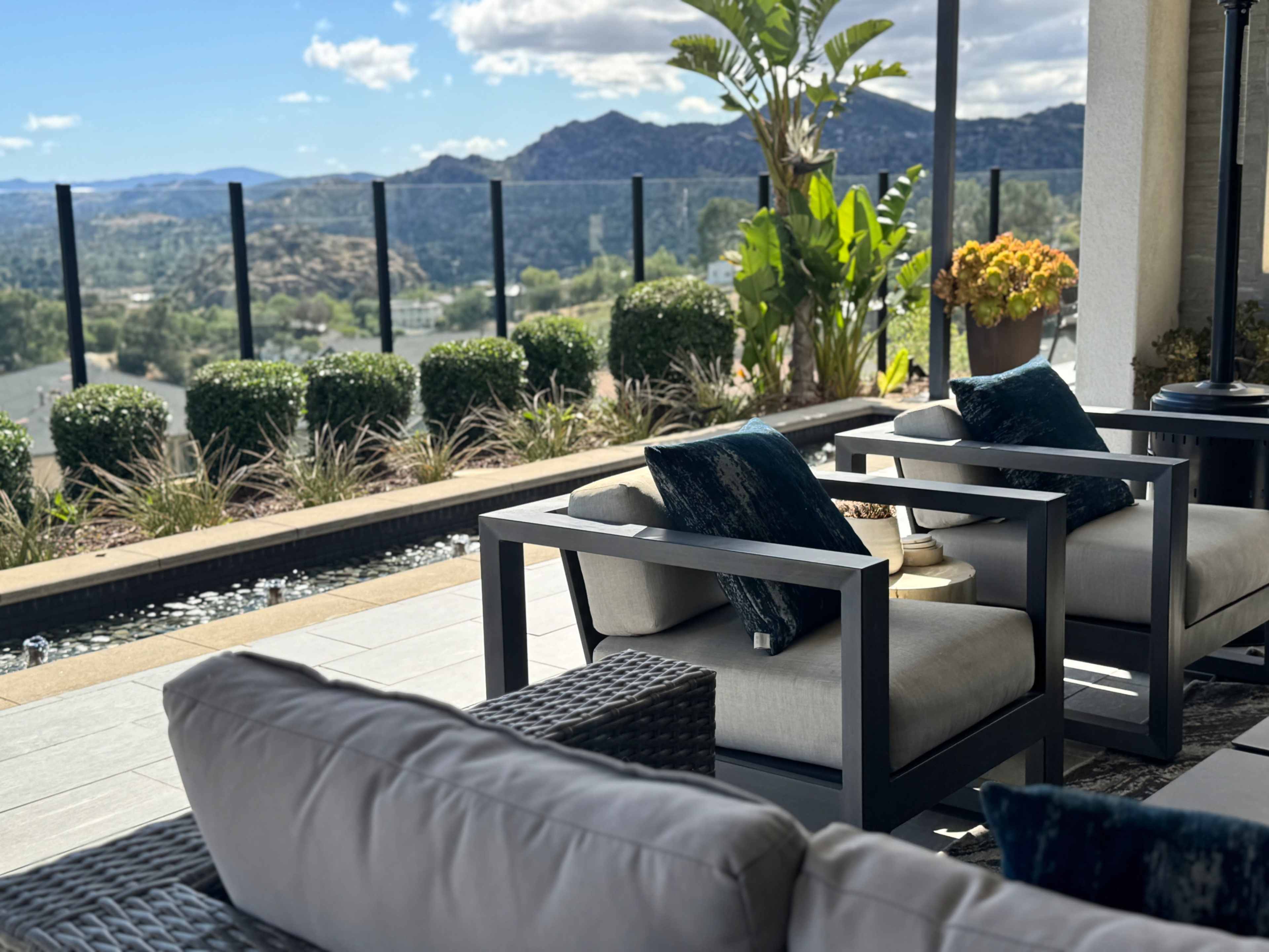 A modern outdoor seating area features black and gray furniture with cushions, overlooking a landscaped view of rolling hills and greenery.
