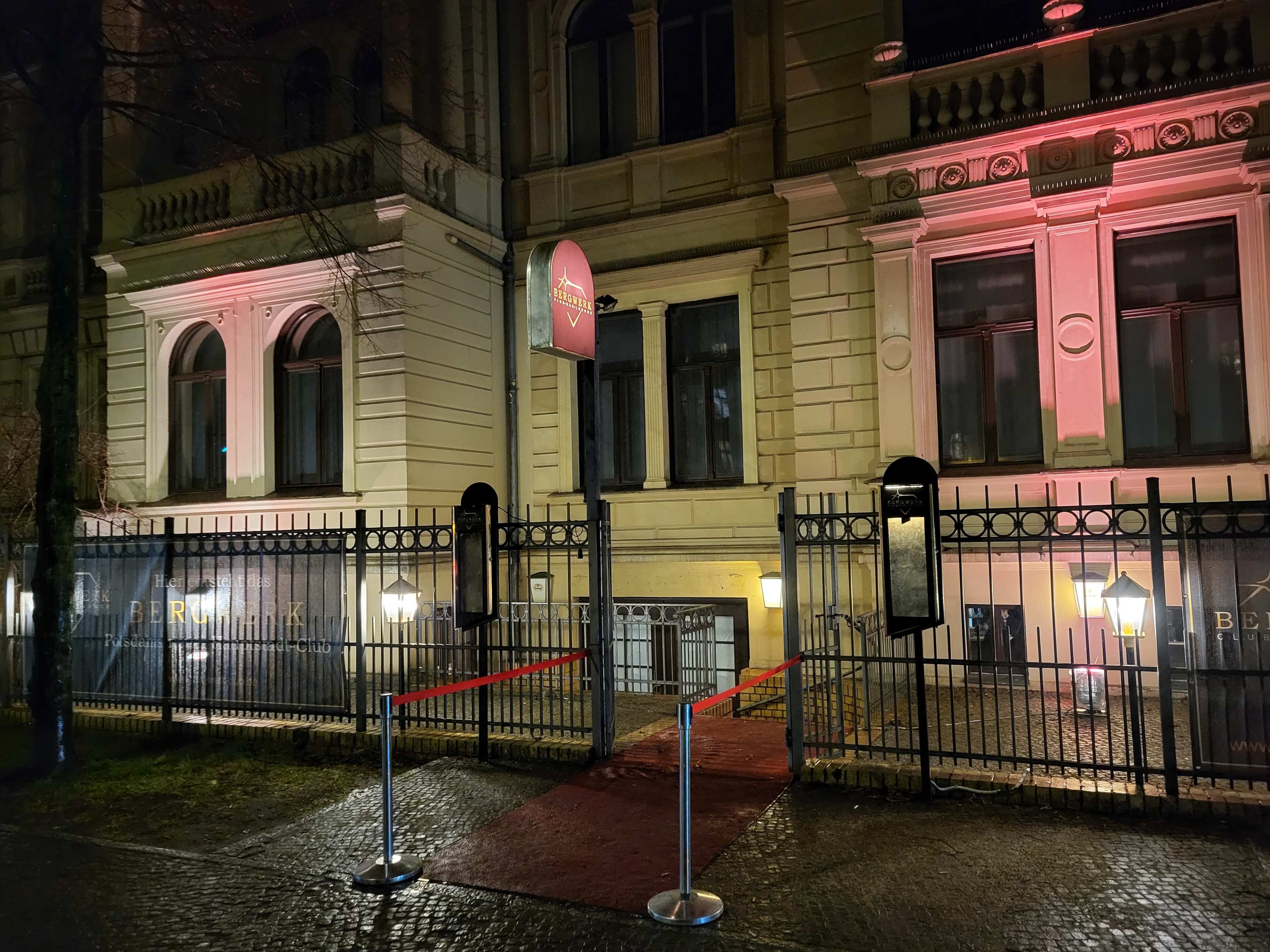 The entrance of a building is framed by a gated area with red ropes and illuminated lanterns, featuring a sign that reads "Bergmark."