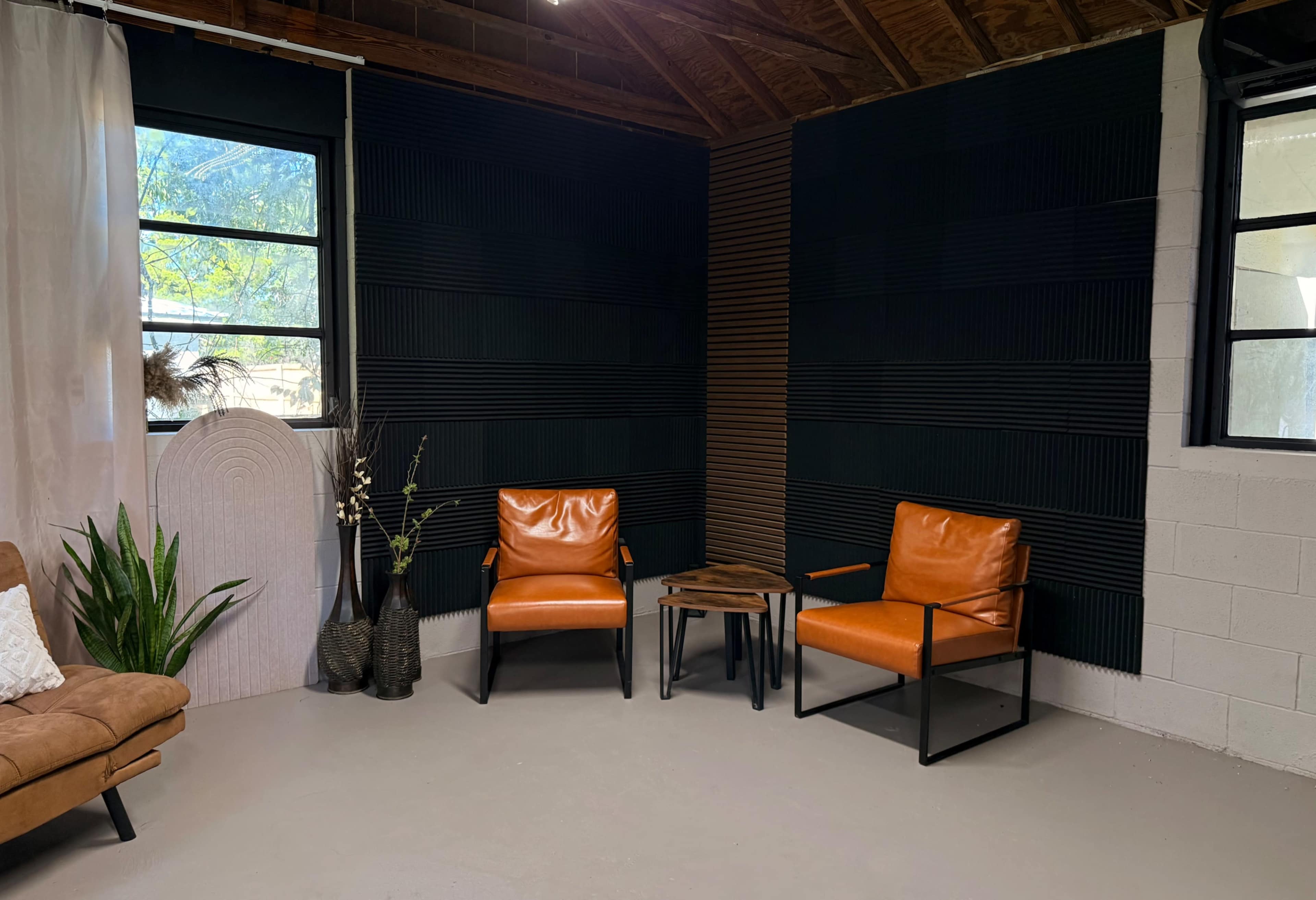 The image shows a corner of a room with two orange chairs, a small wooden table, a decorative plant, and textured black walls.