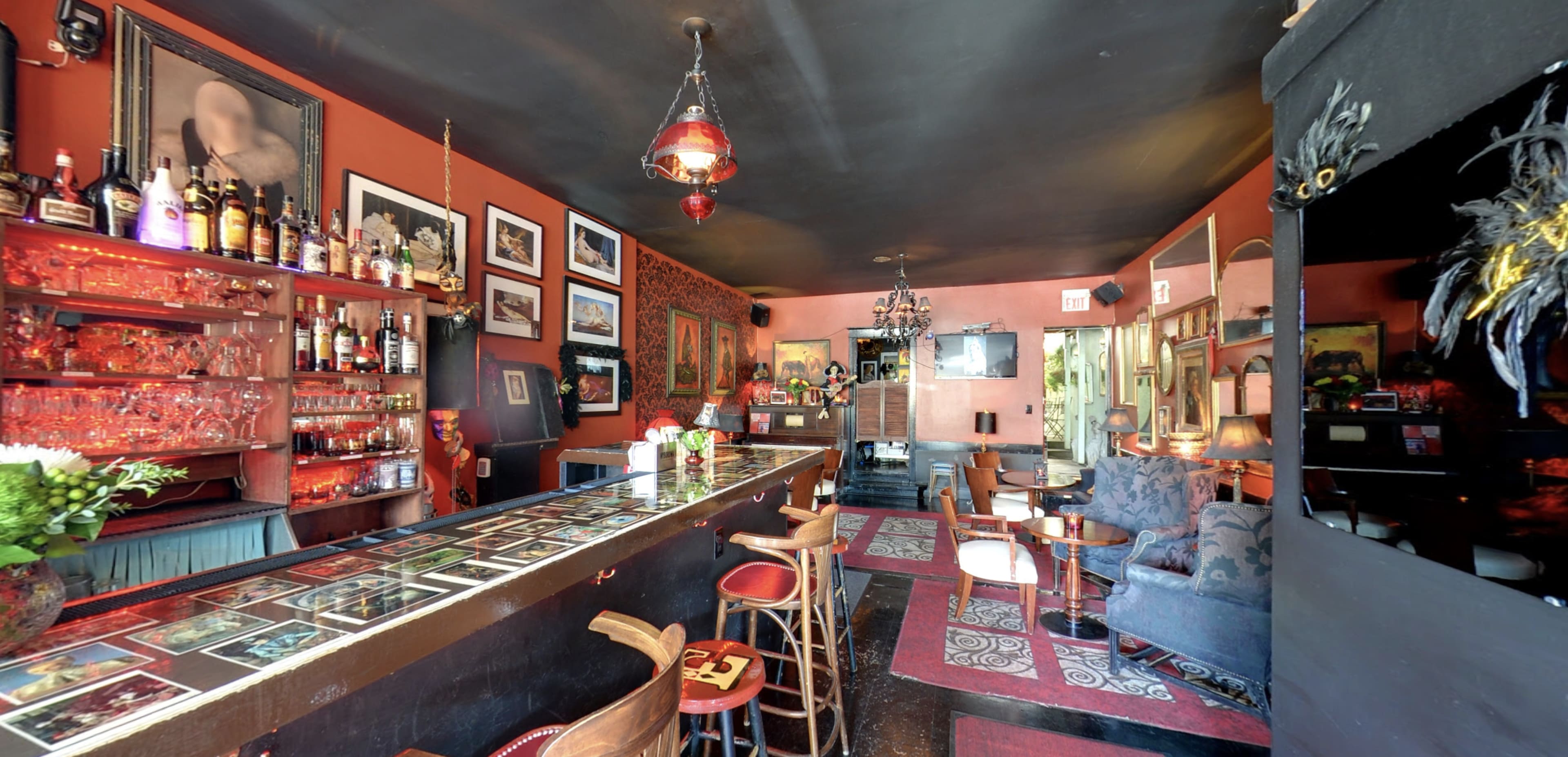 A dimly lit bar with a long counter, shelves of liquor, and various artwork adorning the walls.
