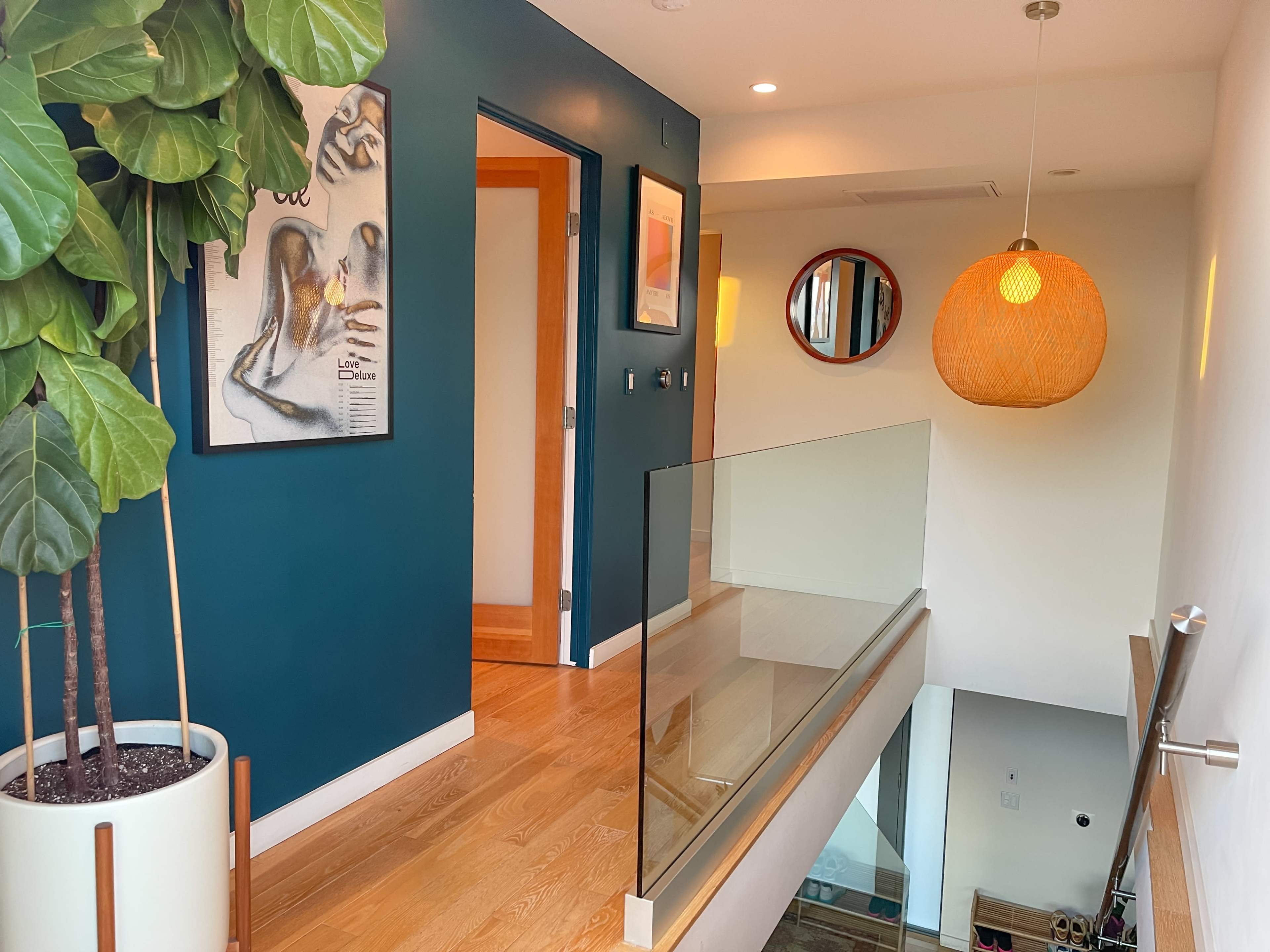 A modern hallway featuring a green accent wall, a potted plant, and a glass railing overlooking a lower level.