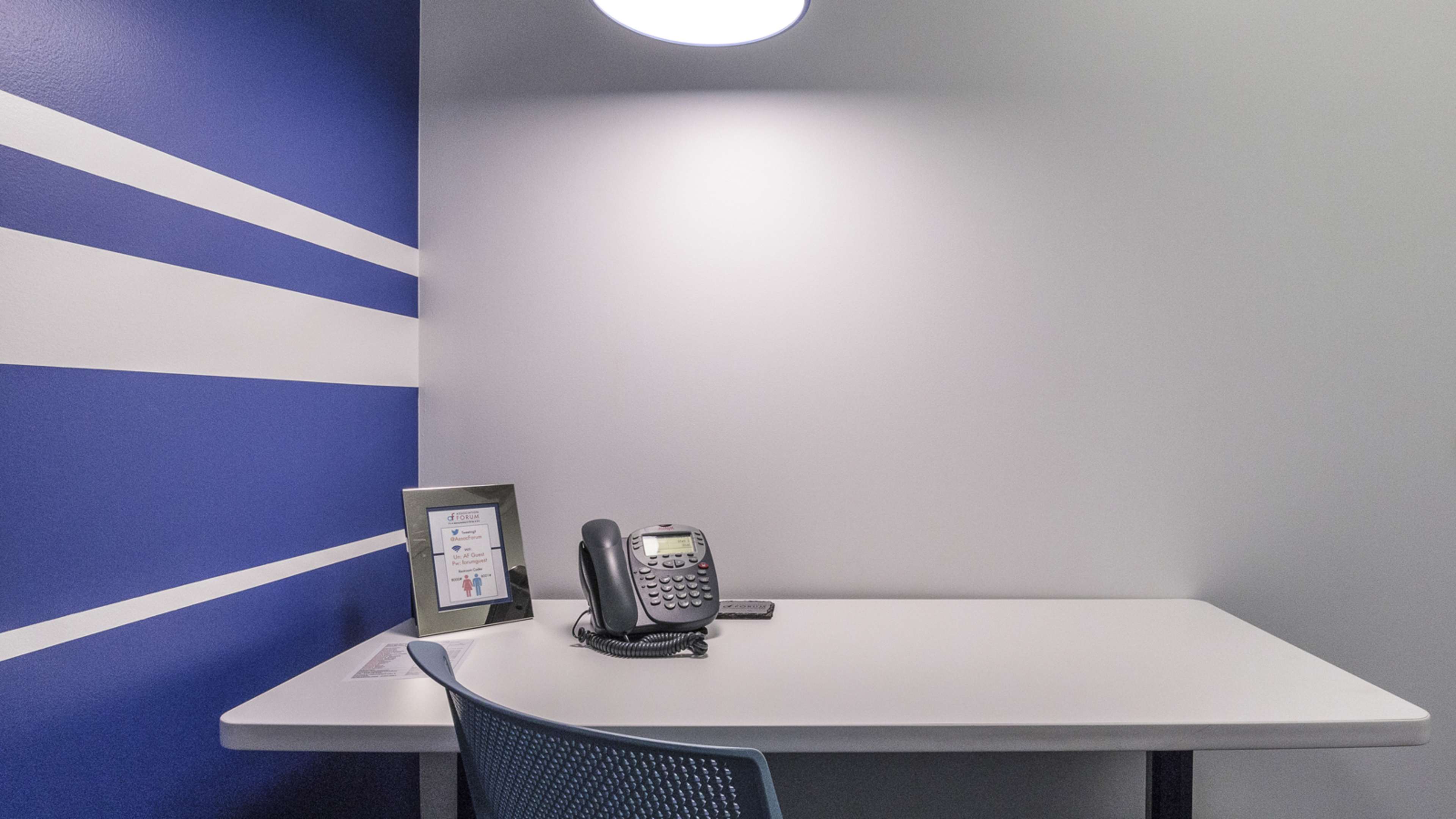 A desk with a telephone and a framed certificate against a backdrop of a blue and gray wall.