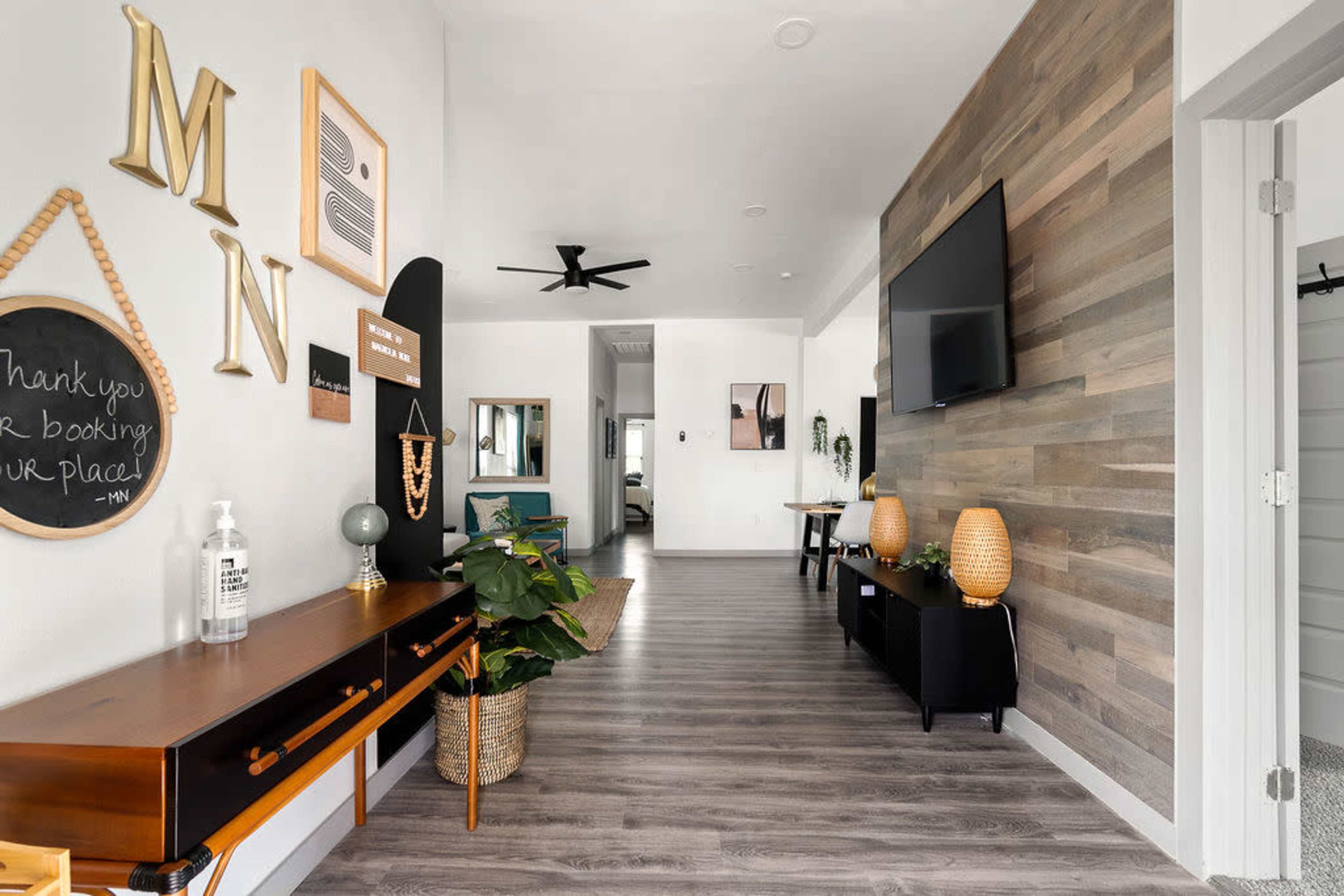 A modern hallway featuring wood paneling, a console table with decorative items, and a TV mounted on the wall.