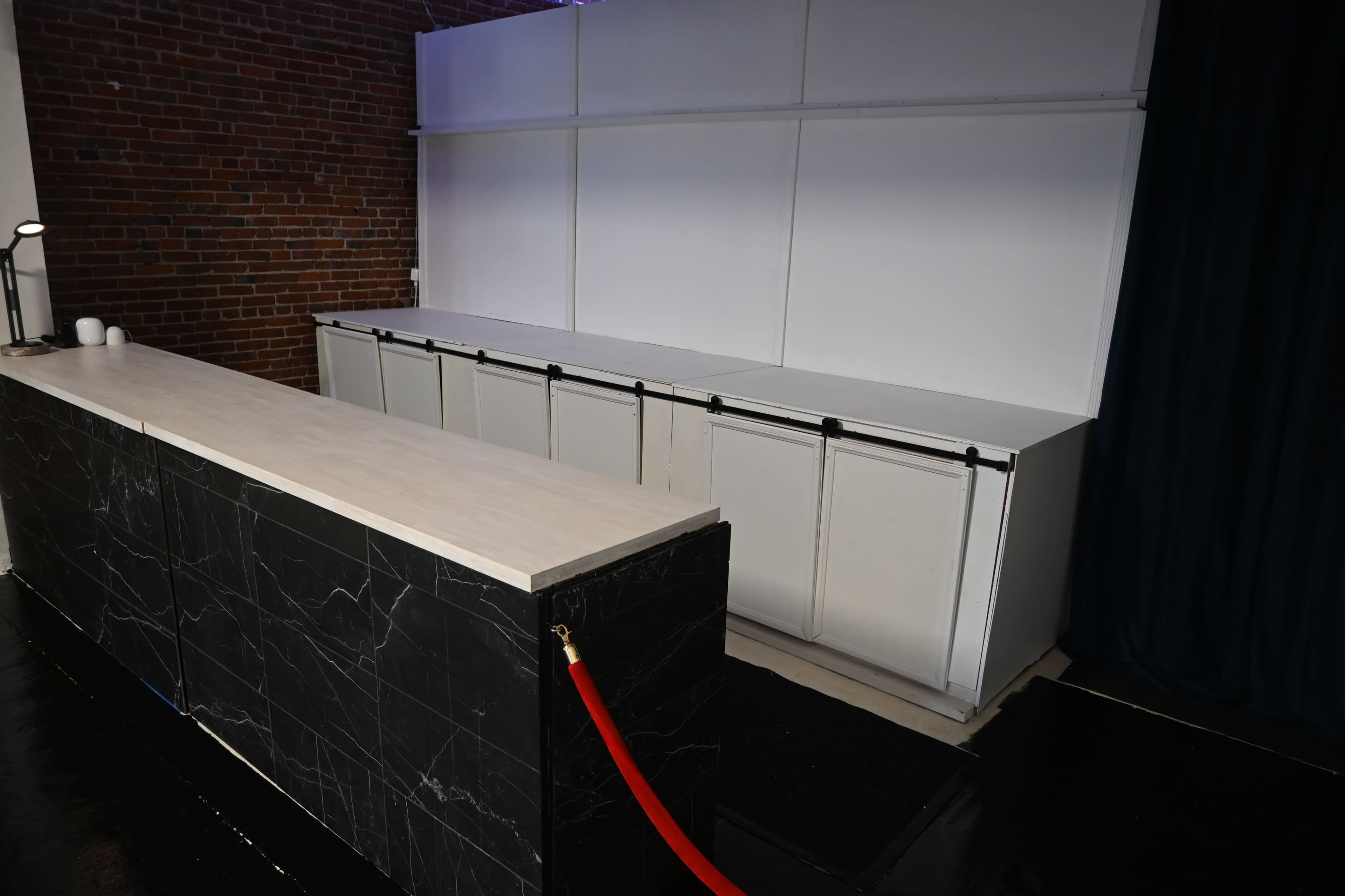 The image shows a minimalist reception area with a black marble countertop and a row of white cabinets against a plain backdrop.