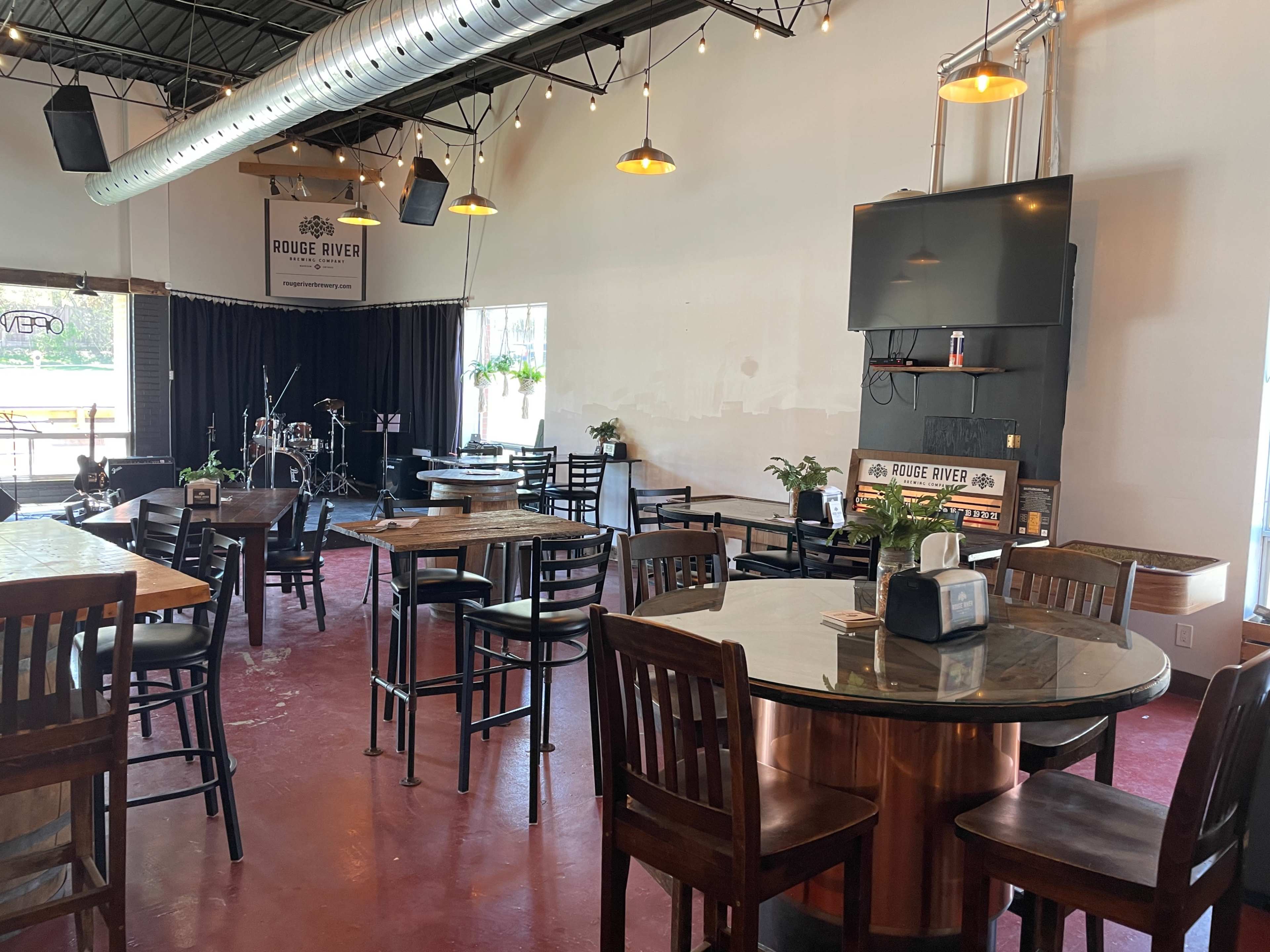 A spacious venue with tables and chairs arranged for dining, and a small stage area featuring musical equipment.