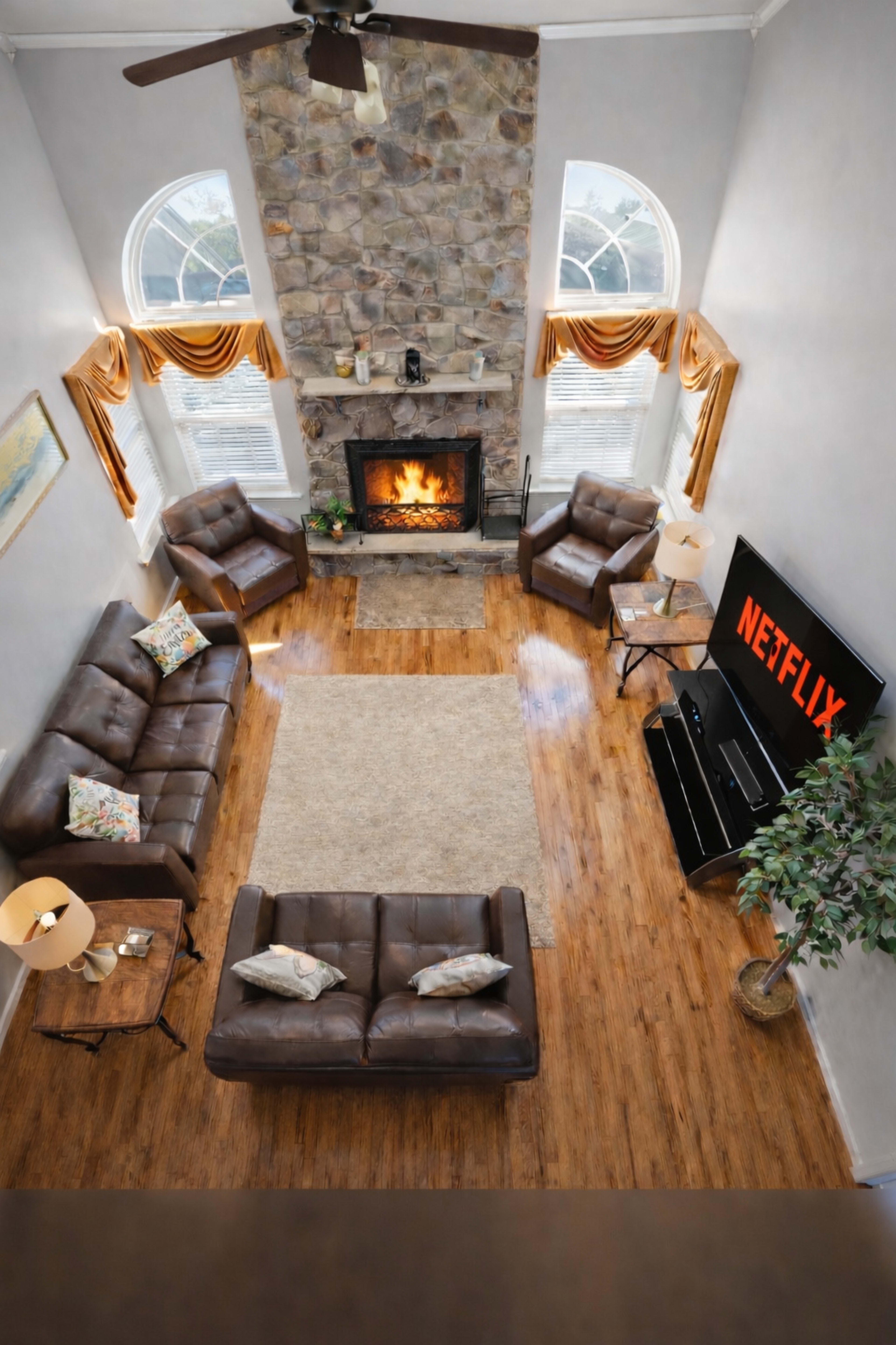 The image shows a living room with a stone fireplace, two brown leather sofas, a coffee table, and a television displaying the Netflix logo.