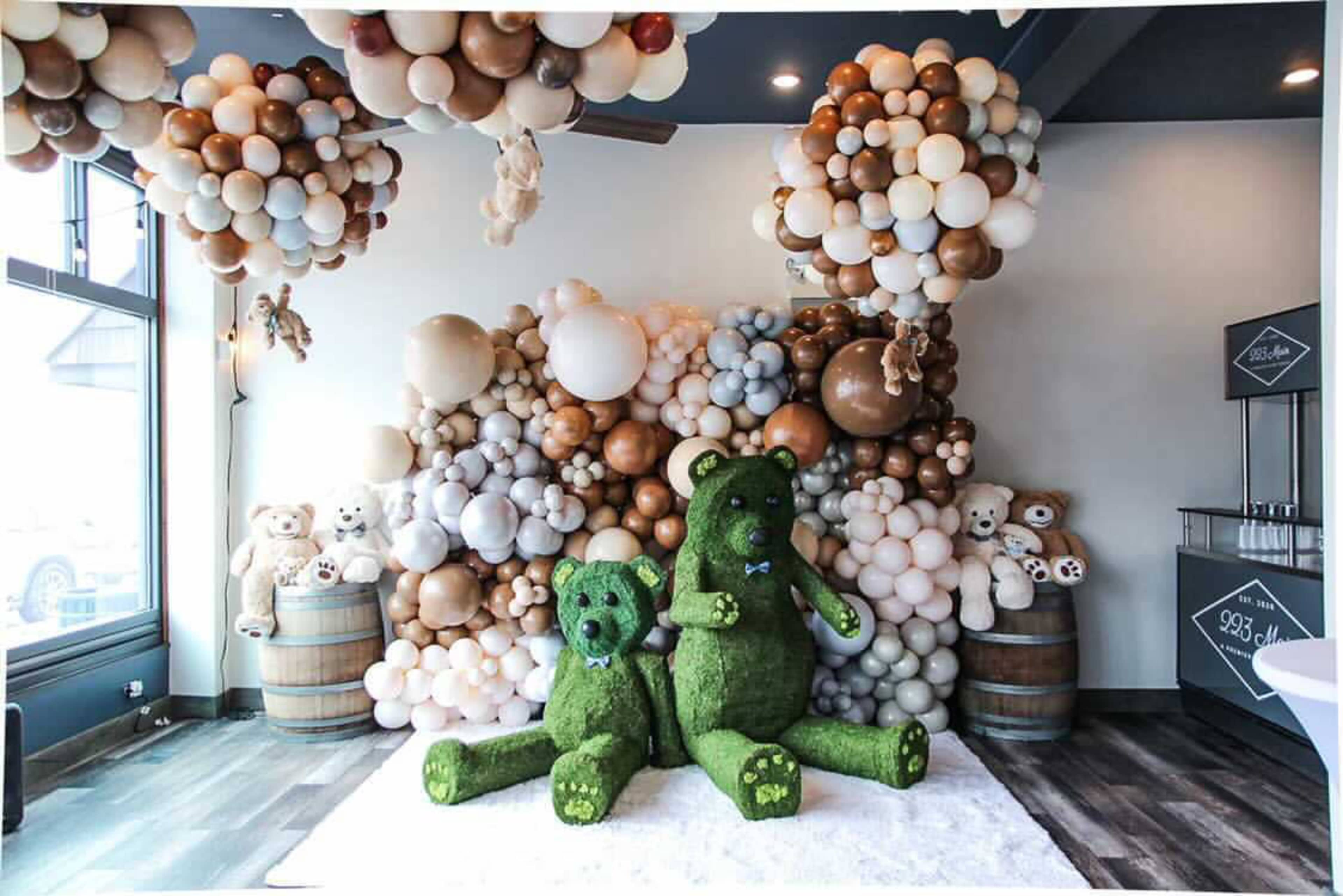 A decorated event space featuring two large green teddy bear figures sitting in front of a backdrop of balloon arrangements in various colors and shapes.