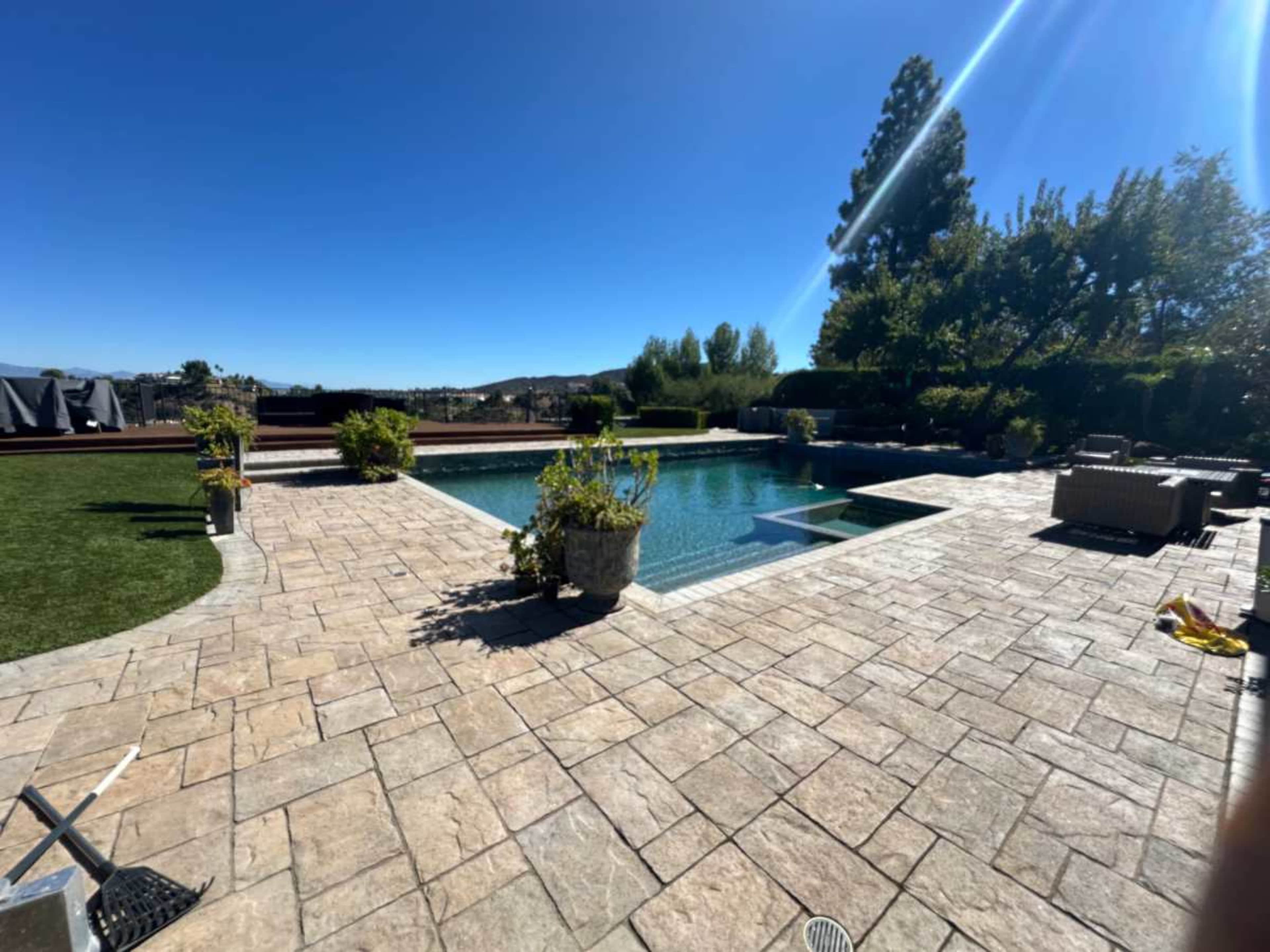 The image shows a large backyard with a swimming pool surrounded by patio pavers and landscaped greenery.