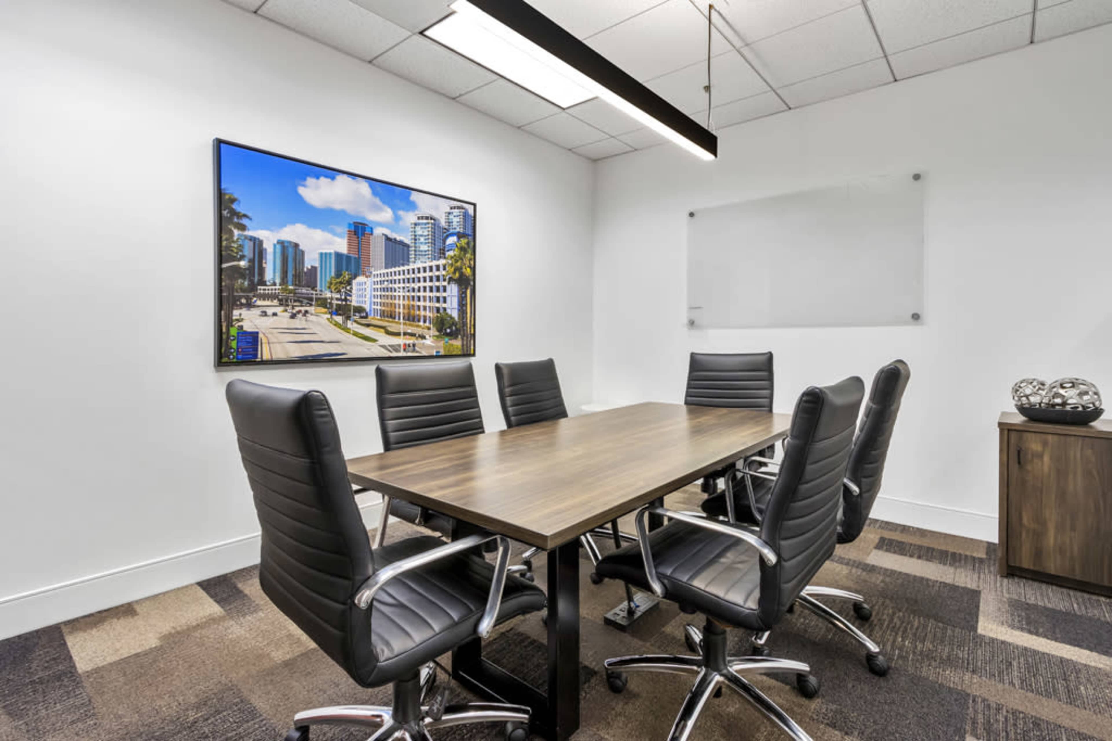 A modern conference room features a long wooden table surrounded by six black leather chairs, with a large cityscape artwork on the wall.