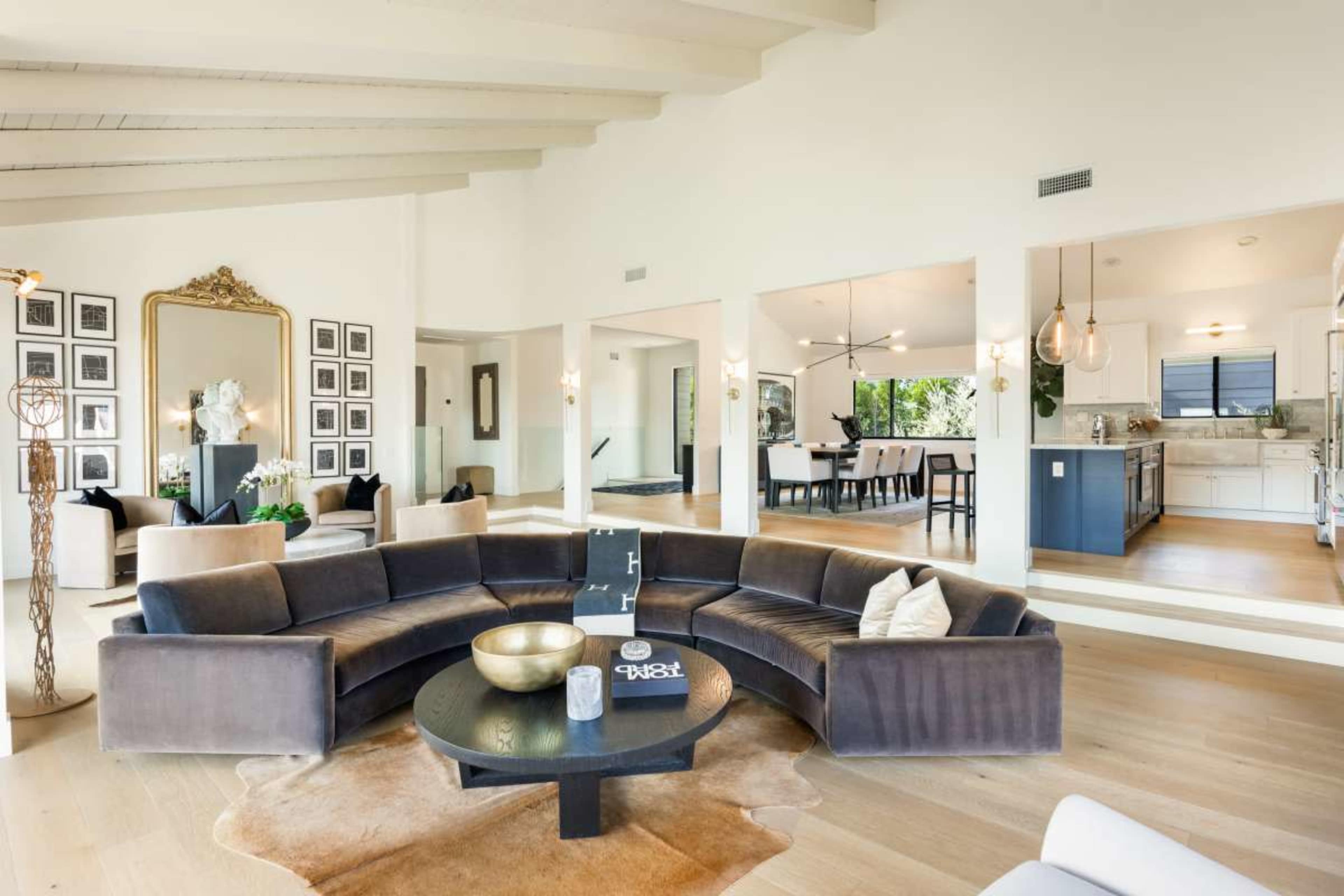 The image shows a spacious living room with a curved sectional sofa, a round coffee table, and an open layout leading to a dining area and kitchen.
