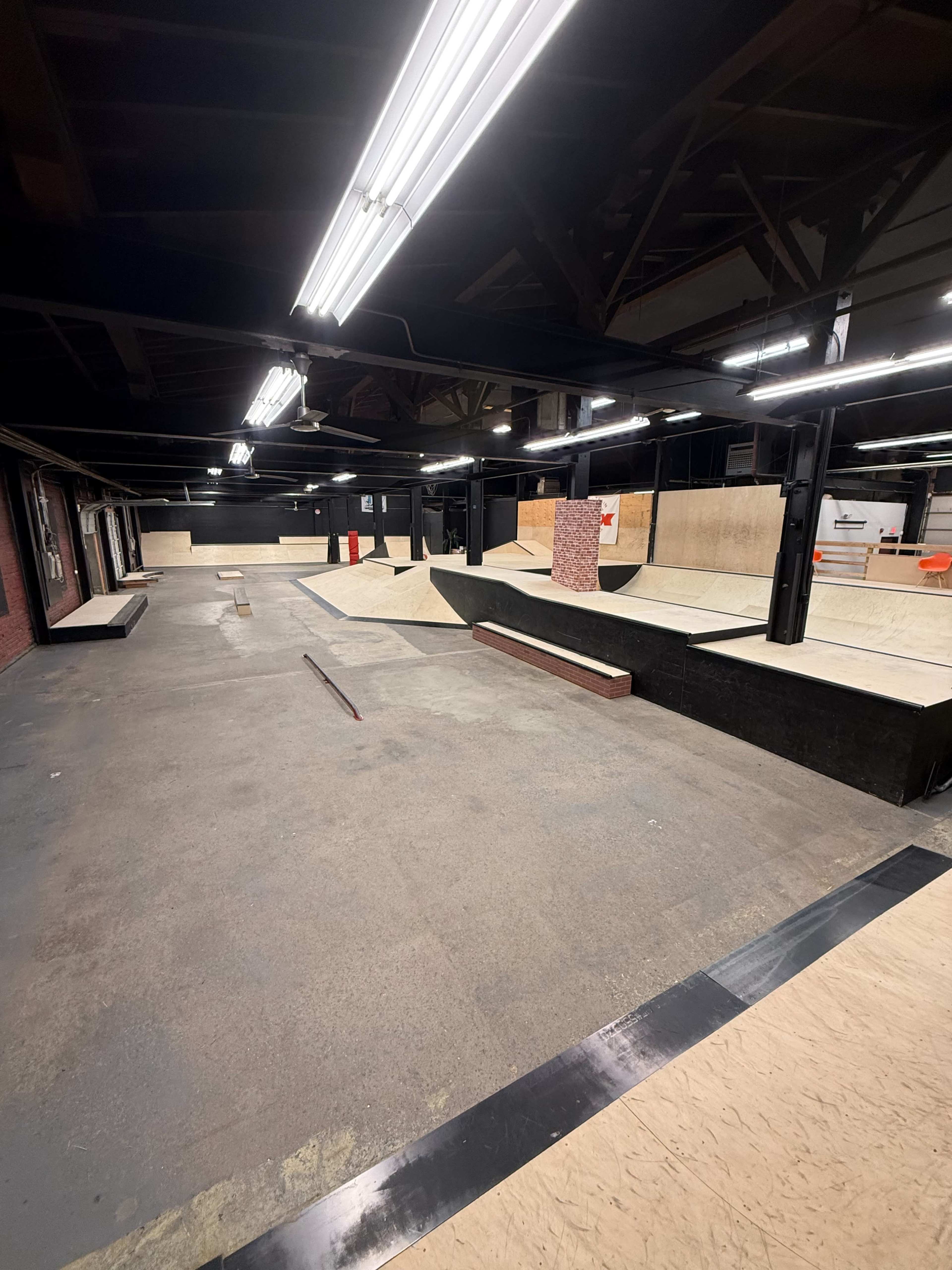 The image shows a spacious indoor skate park featuring various ramps, rails, and flat surfaces for skating.