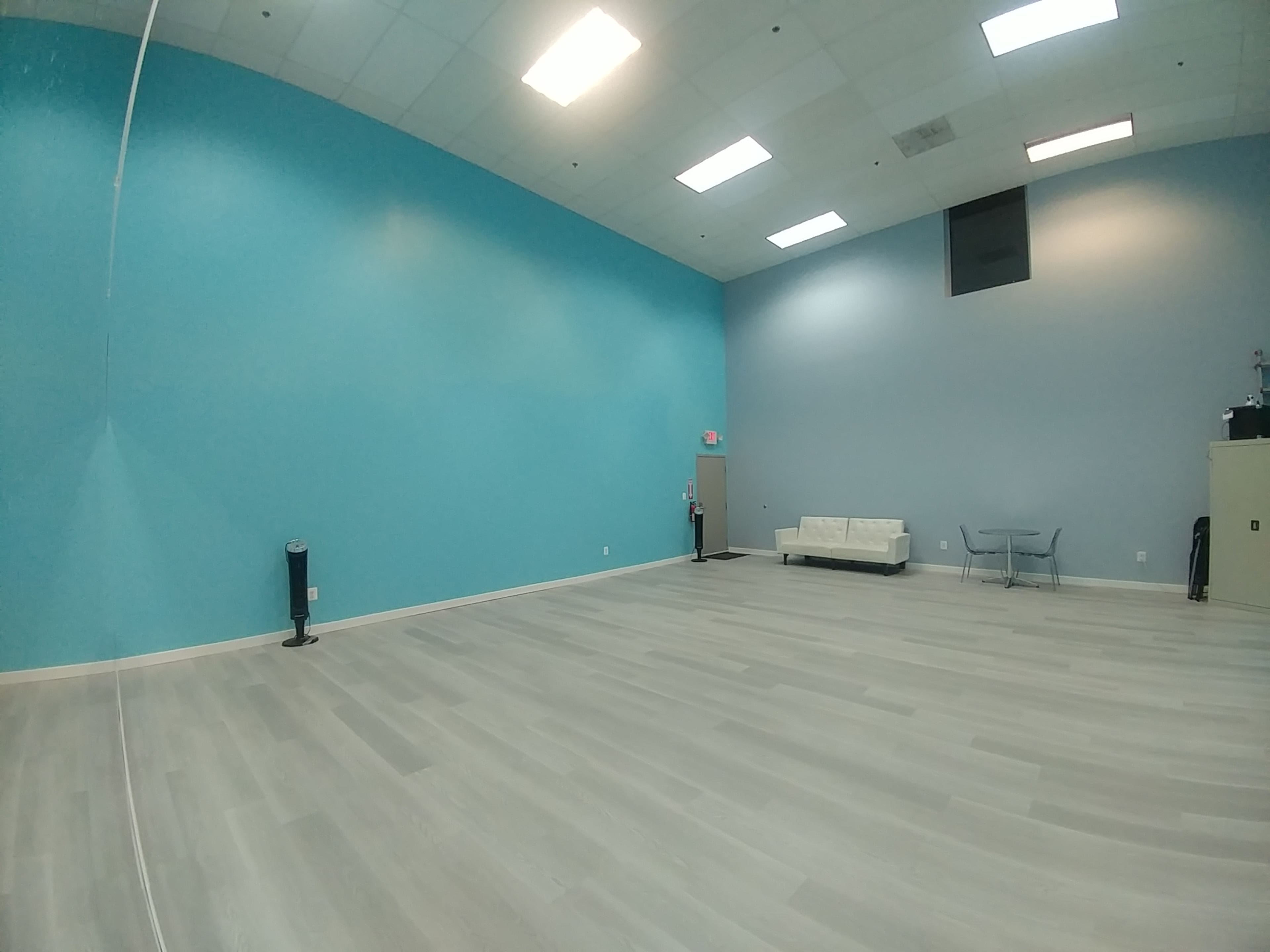 An empty room with light gray flooring, a turquoise wall, a white sofa, and a small table.
