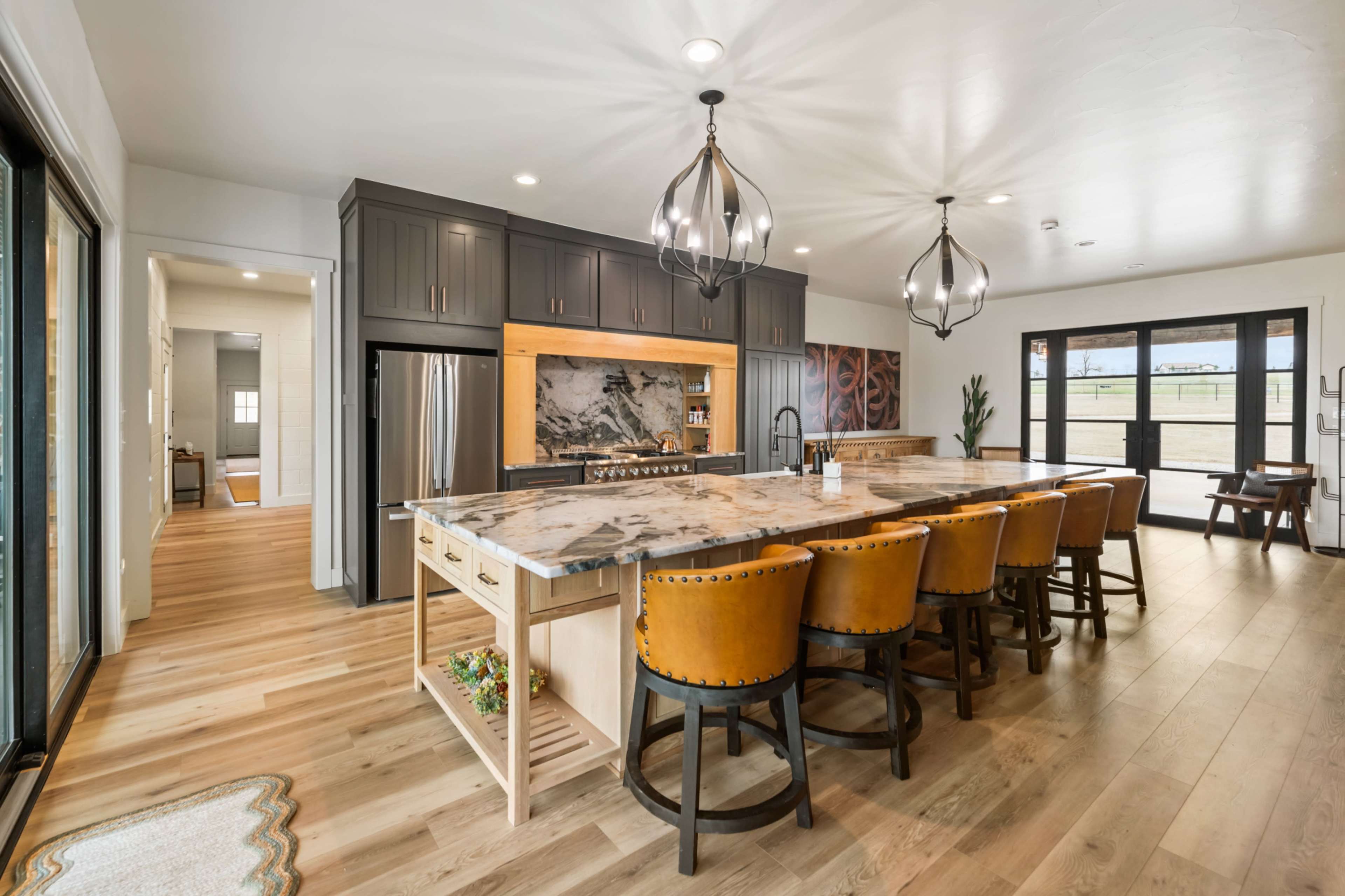 The image shows a modern kitchen with a large marble island, dark cabinets, pendant lighting, and wooden floors.