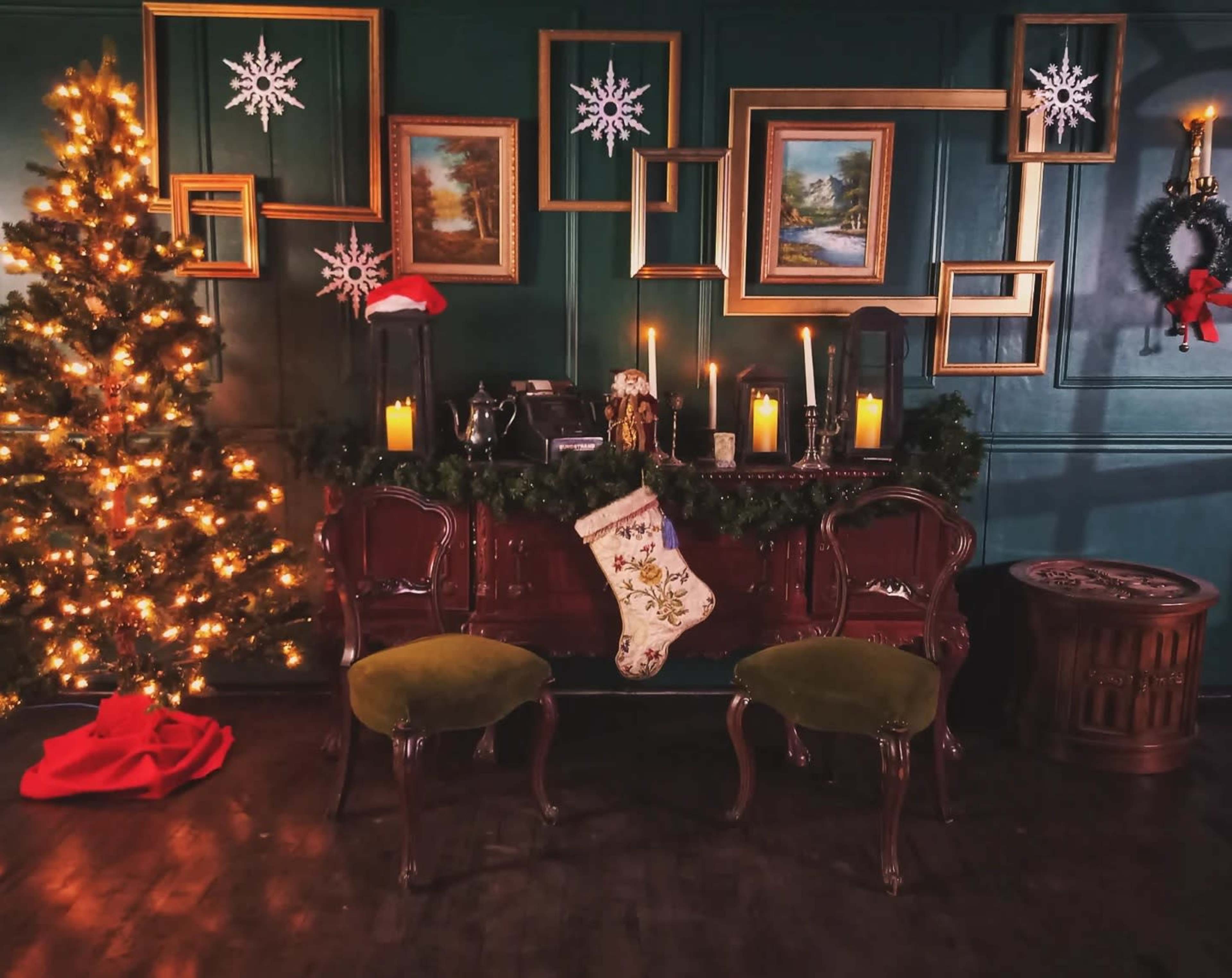 The image depicts a decorated room with a Christmas tree, a console table adorned with candles and garlands, and two green chairs in front of it.