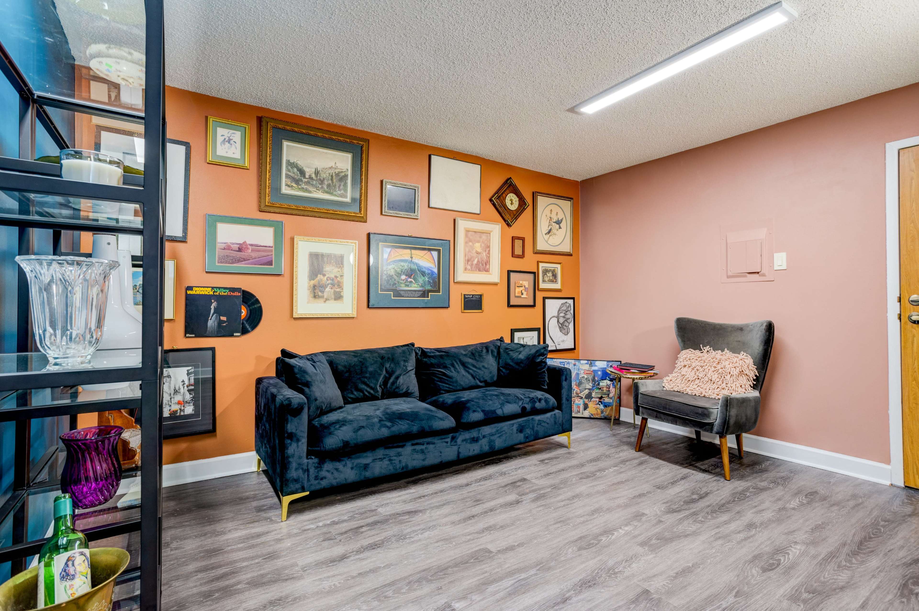 A cozy room features a dark blue couch in front of a wall adorned with various framed artworks and photographs.