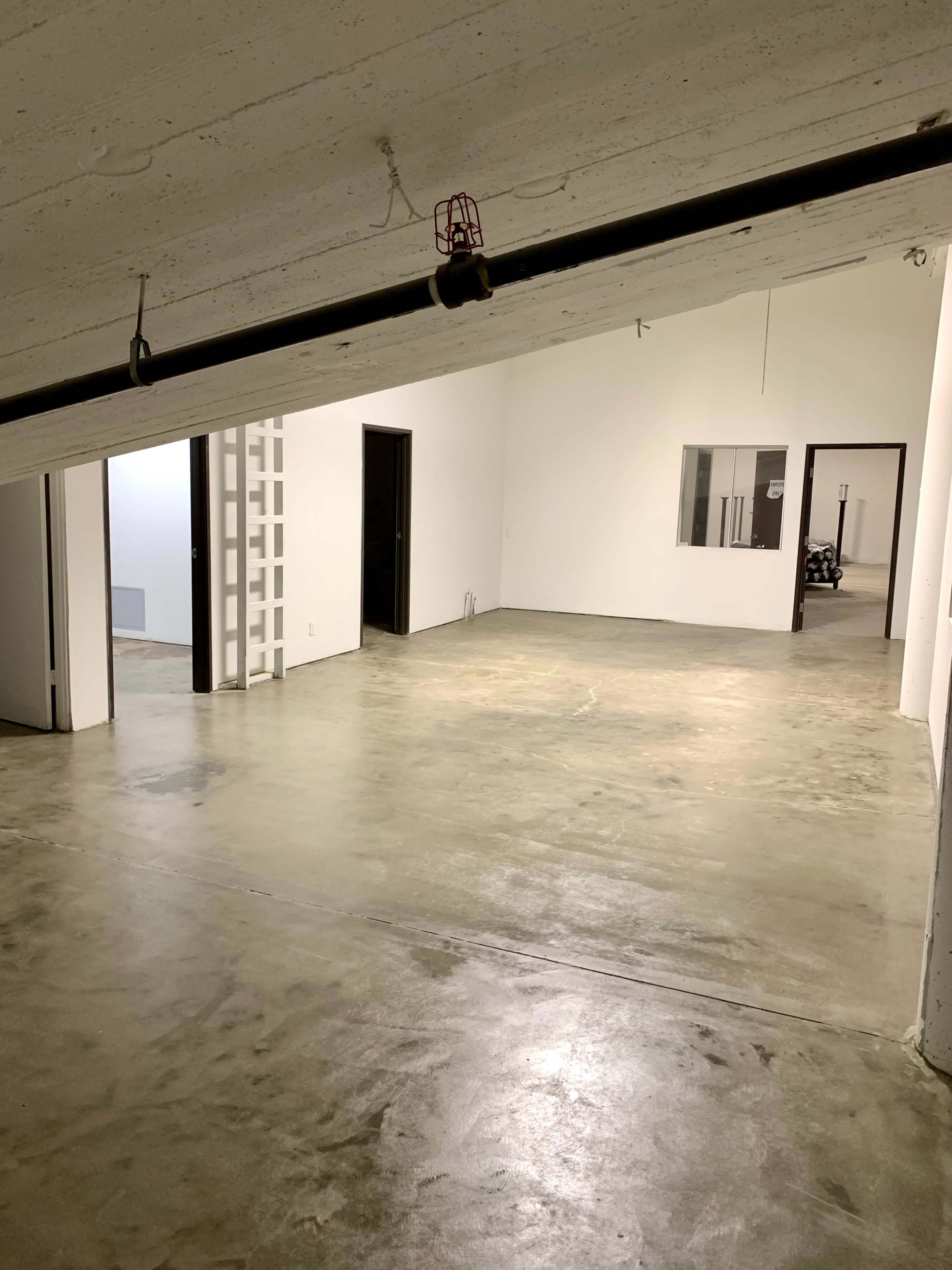 A spacious room with a concrete floor, white walls, and several doorways leading to other areas.