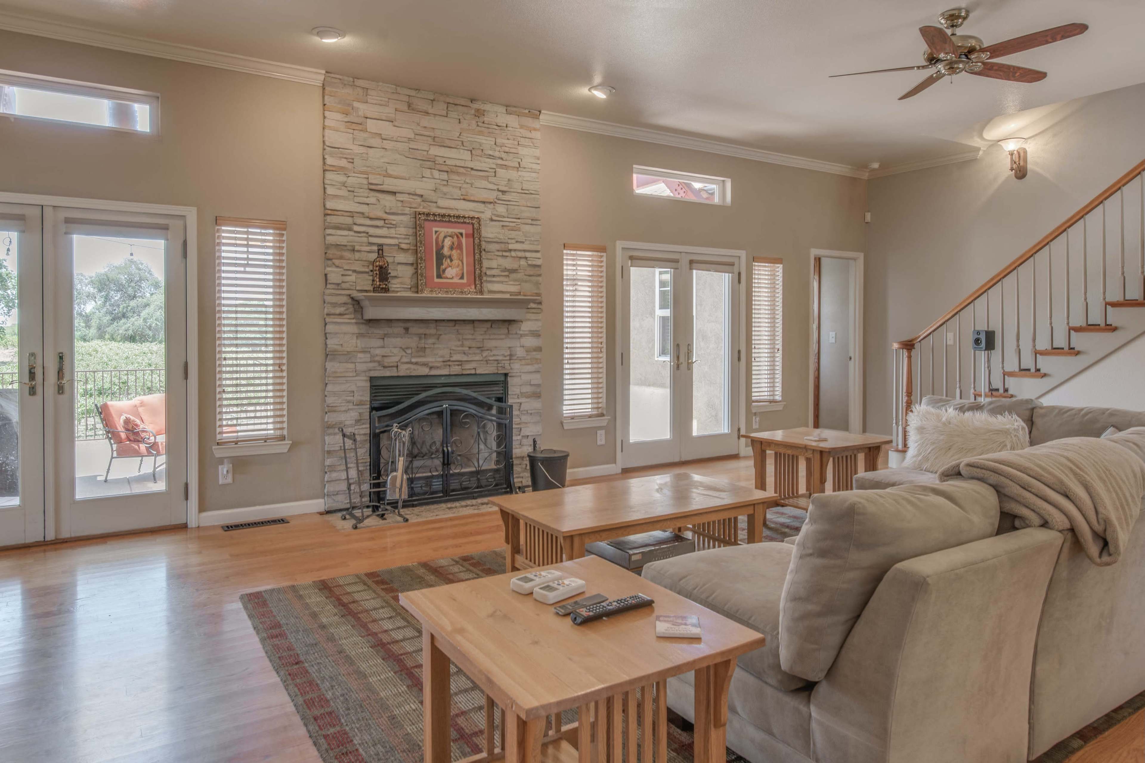 A living room with a stone fireplace, wooden furniture, and large windows that provide natural light.