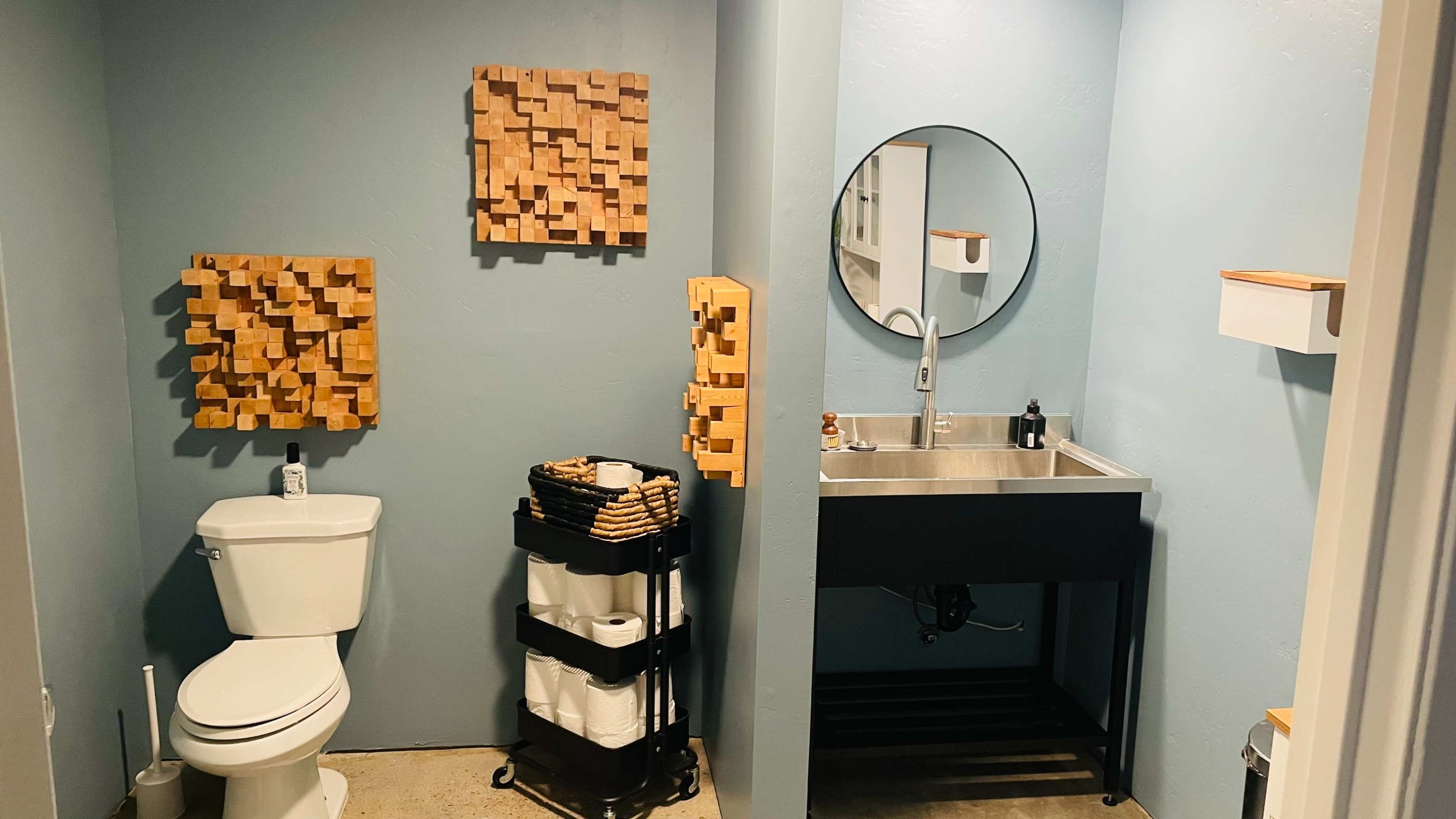 The image shows a modern bathroom featuring a toilet, a sink with a mirror, and decorative wooden wall art.