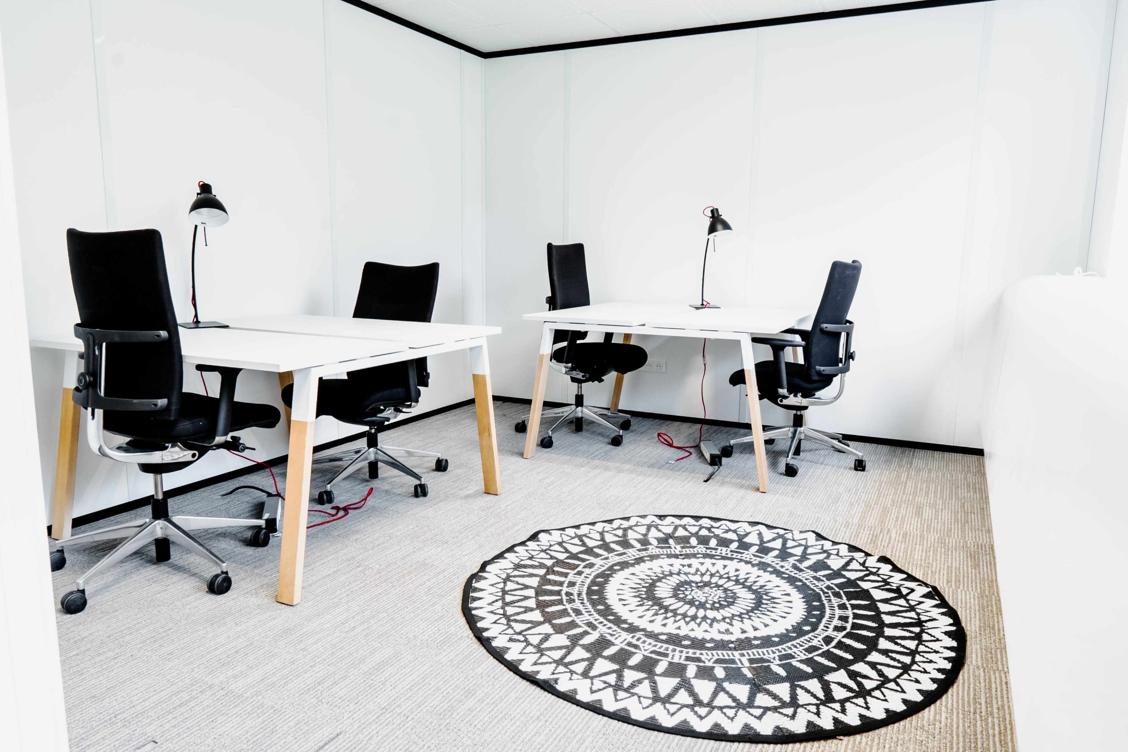The image shows a modern office space with three desks, each paired with a black office chair, and a circular patterned rug on the floor.