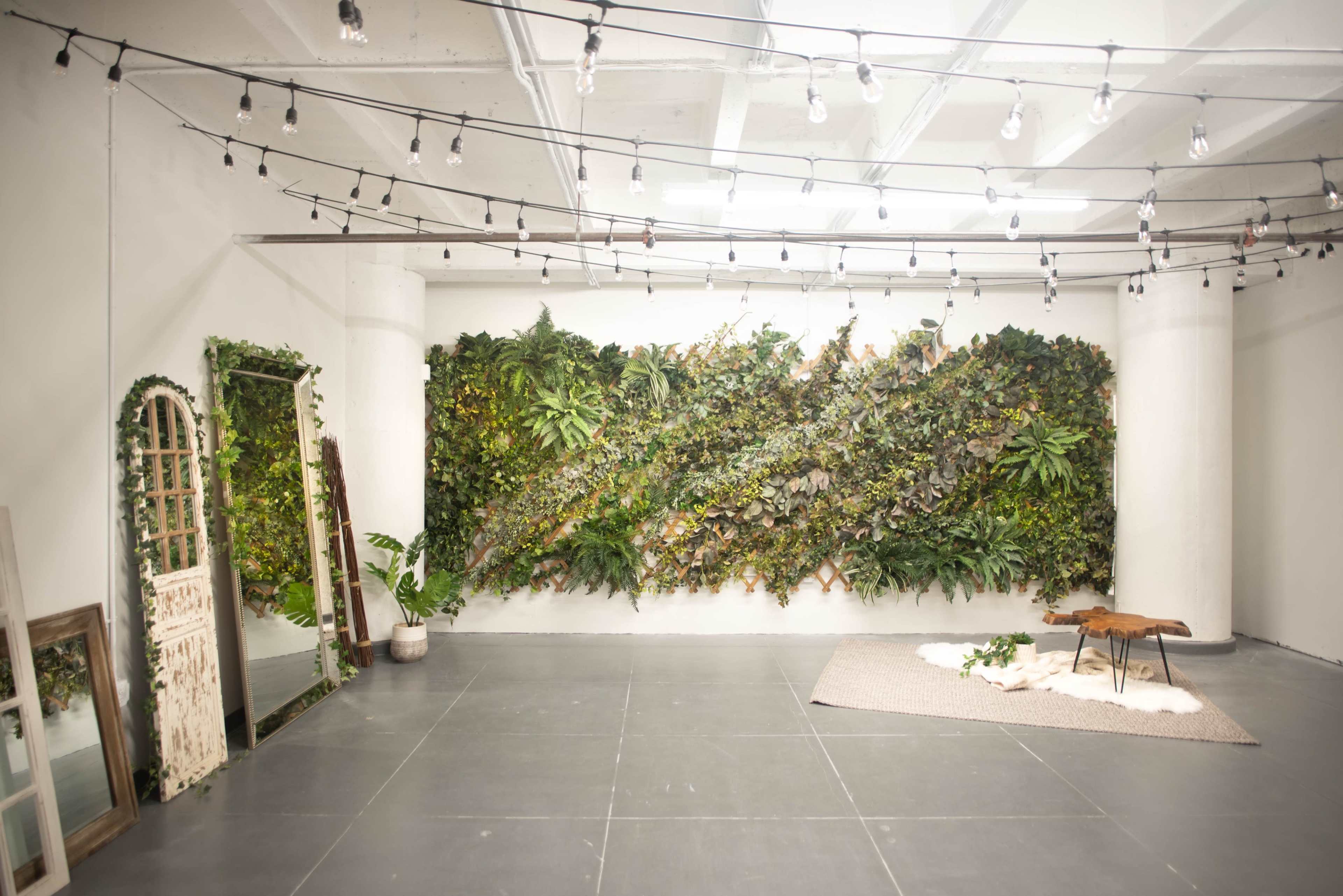 An empty interior space with a vertical garden on one wall, a large mirror, and a small wooden table on a rug.