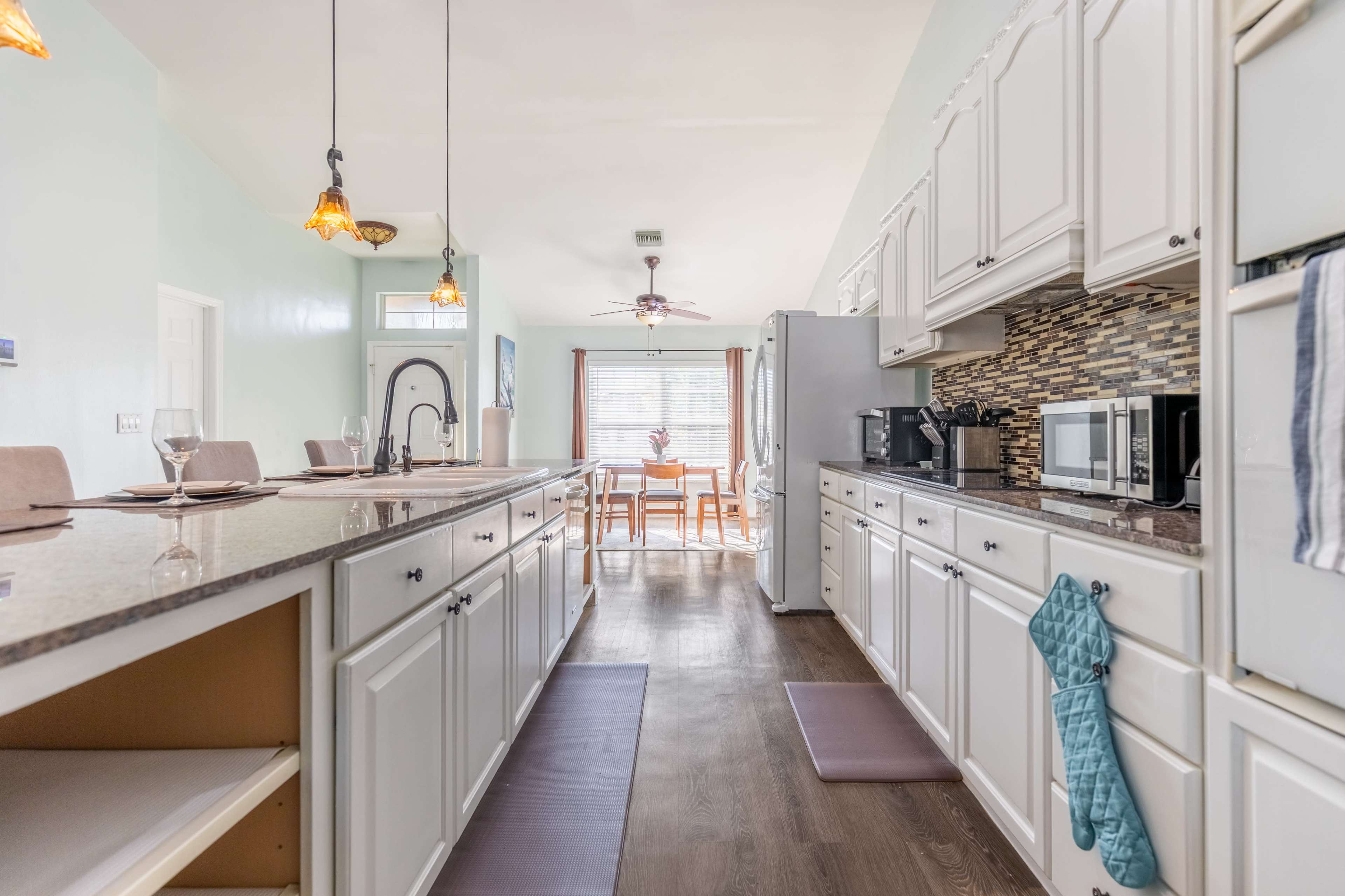 A bright kitchen features white cabinetry, a central island, and a view of an adjoining dining area through a window.