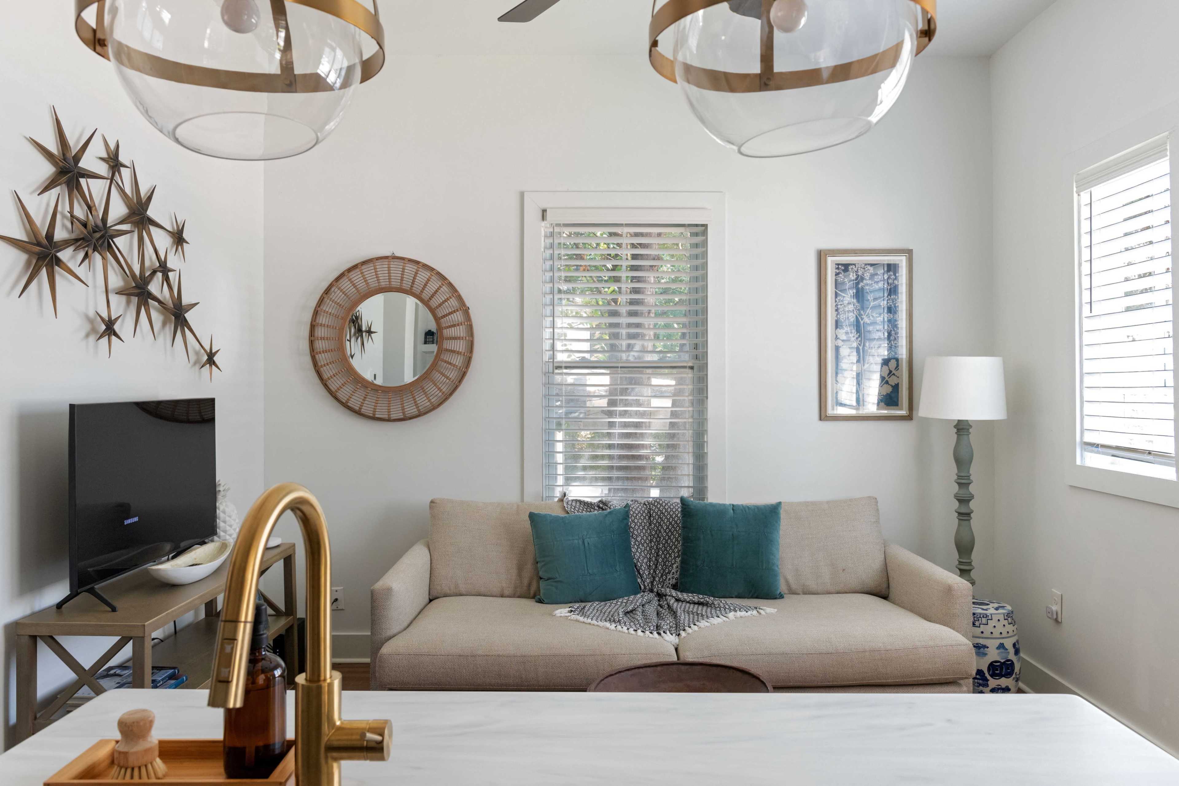 The image shows a modern living room featuring a beige couch with blue cushions, a wall-mounted TV, and decorative star motifs, all arranged under two pendant lights.