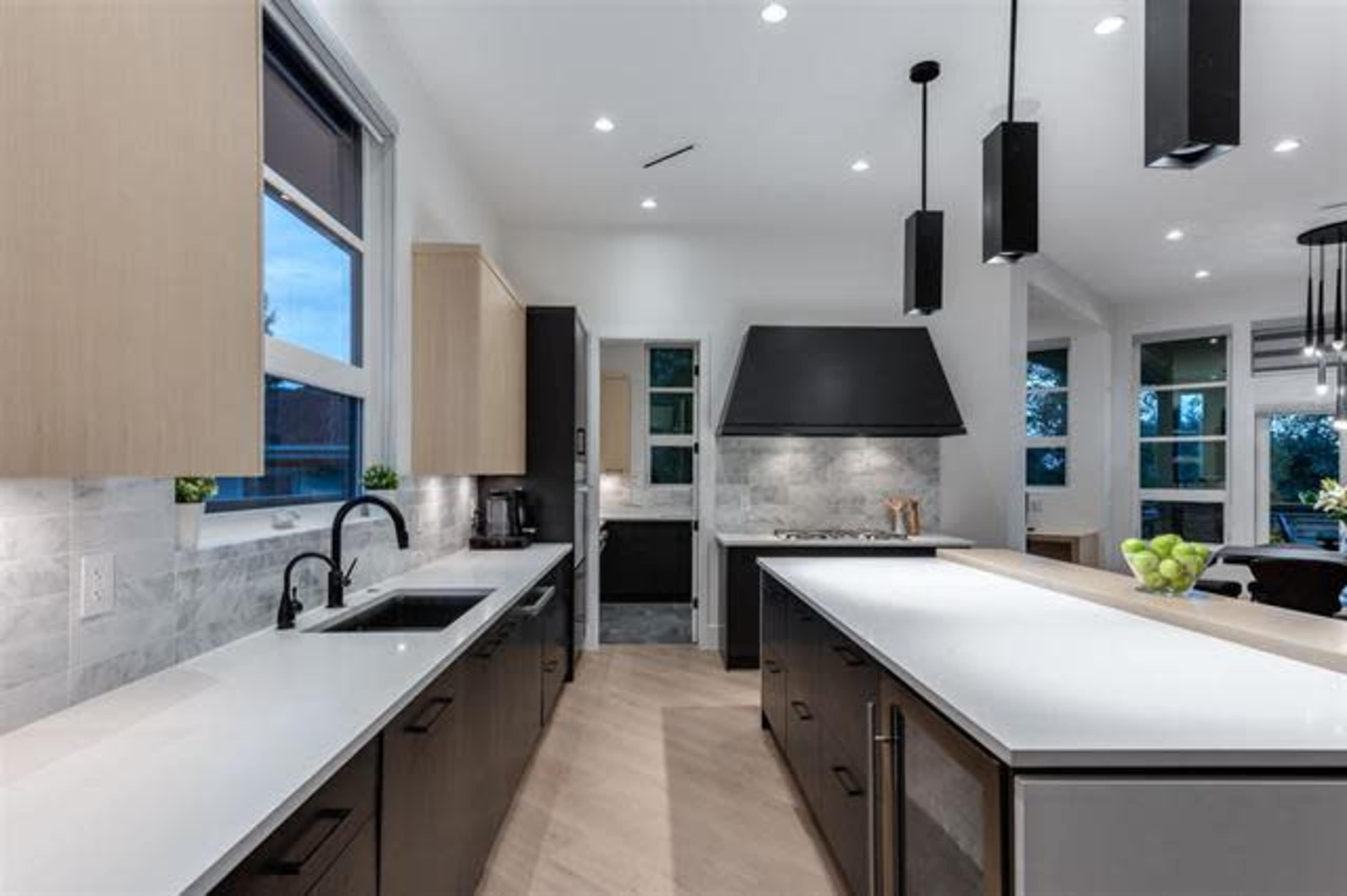 A modern kitchen with a large island, pendant lighting, and a combination of light wood and dark cabinetry.