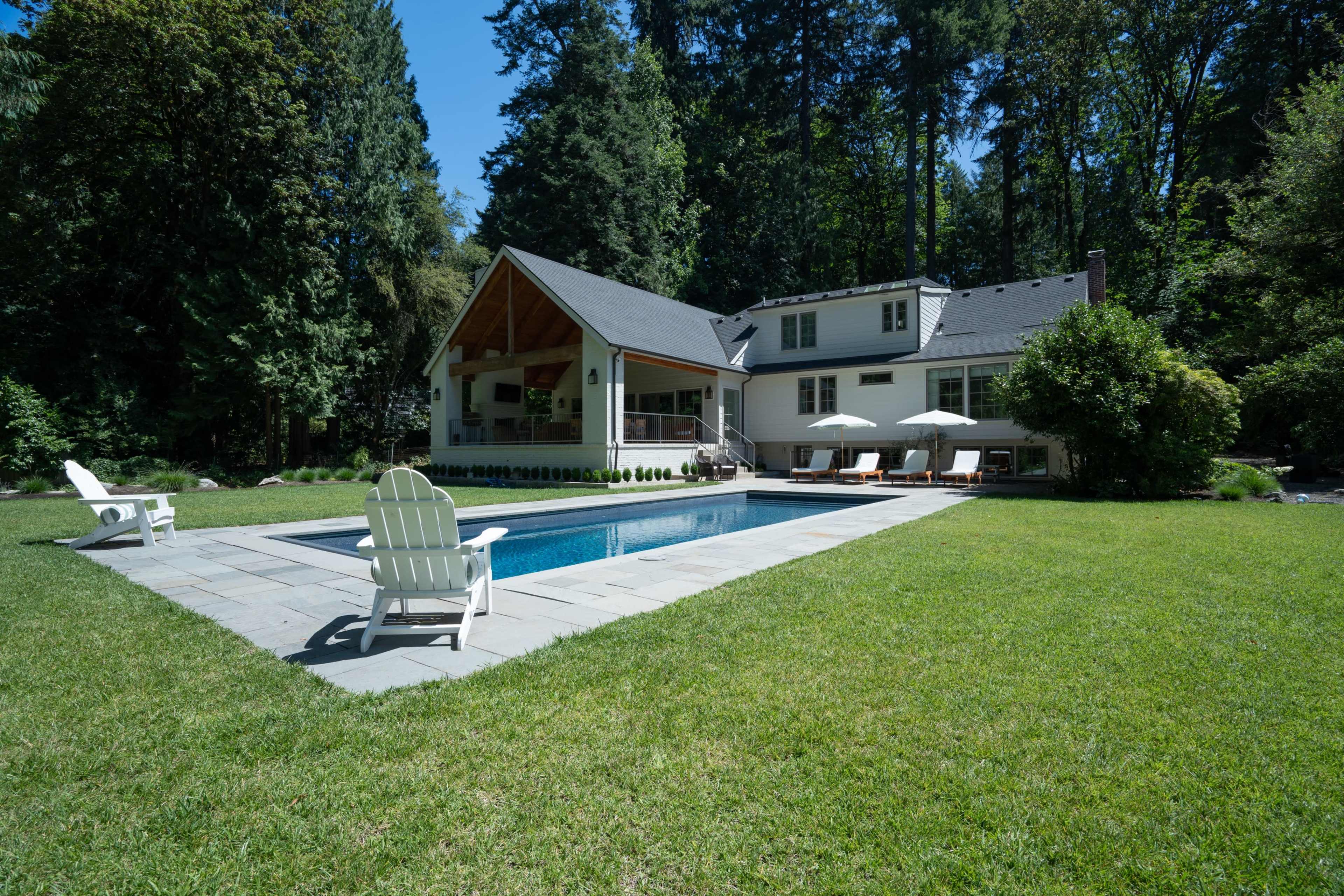 The image shows a modern house with a swimming pool surrounded by landscaped grass and trees.