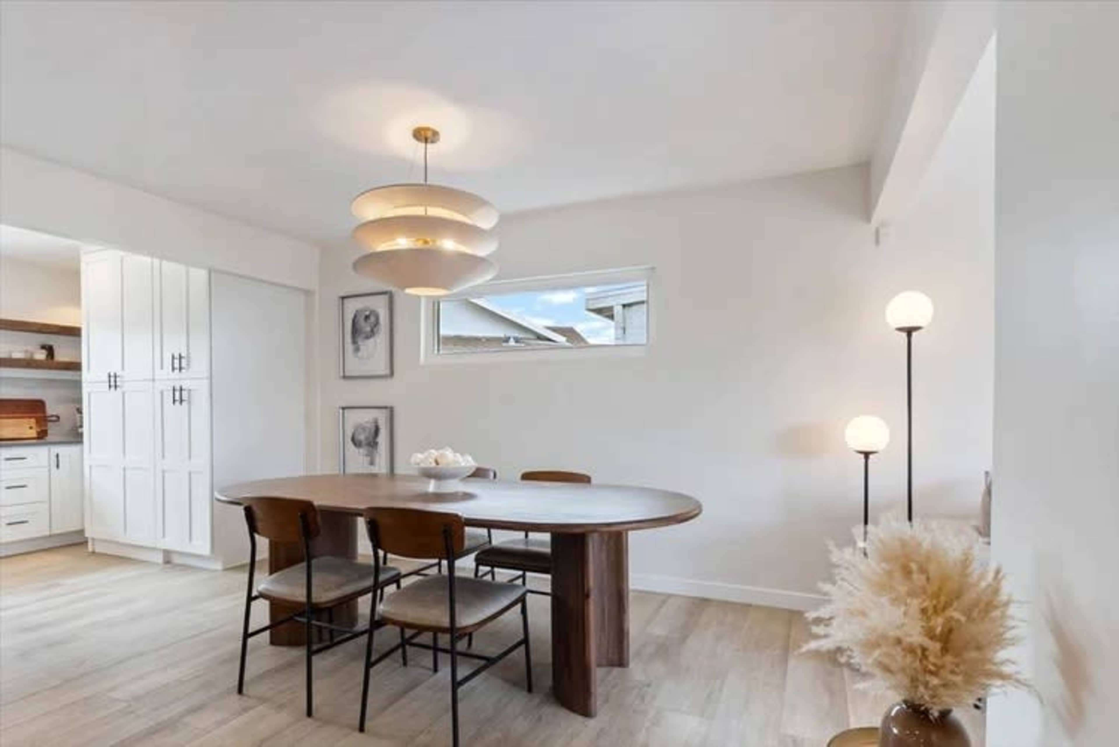 A modern dining area features a round wooden table with four chairs, a pendant light overhead, and a decorative plant in a vase.