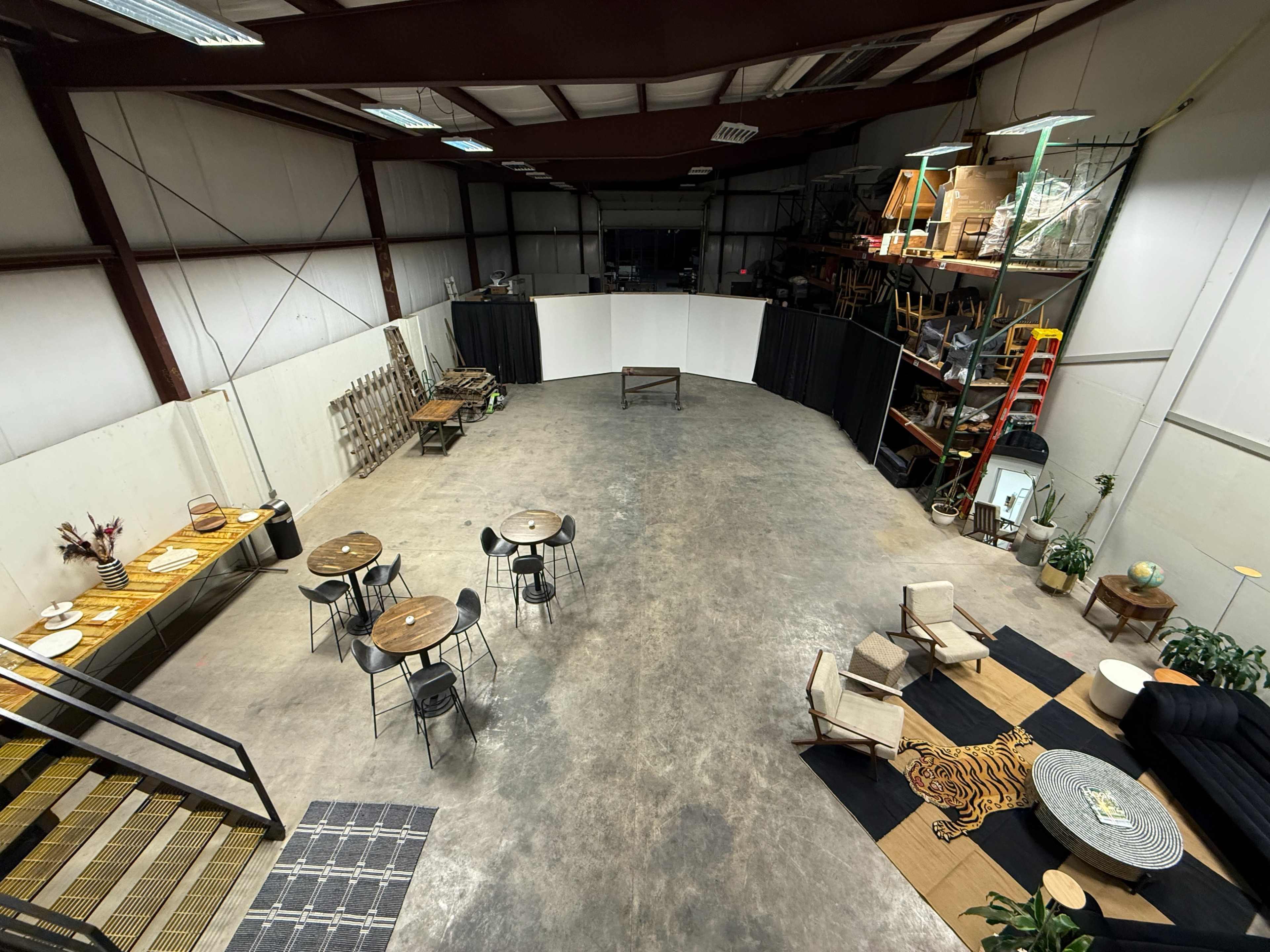 The image shows a spacious indoor venue with seating arrangements, tables, and decor, surrounded by walls and shelving.