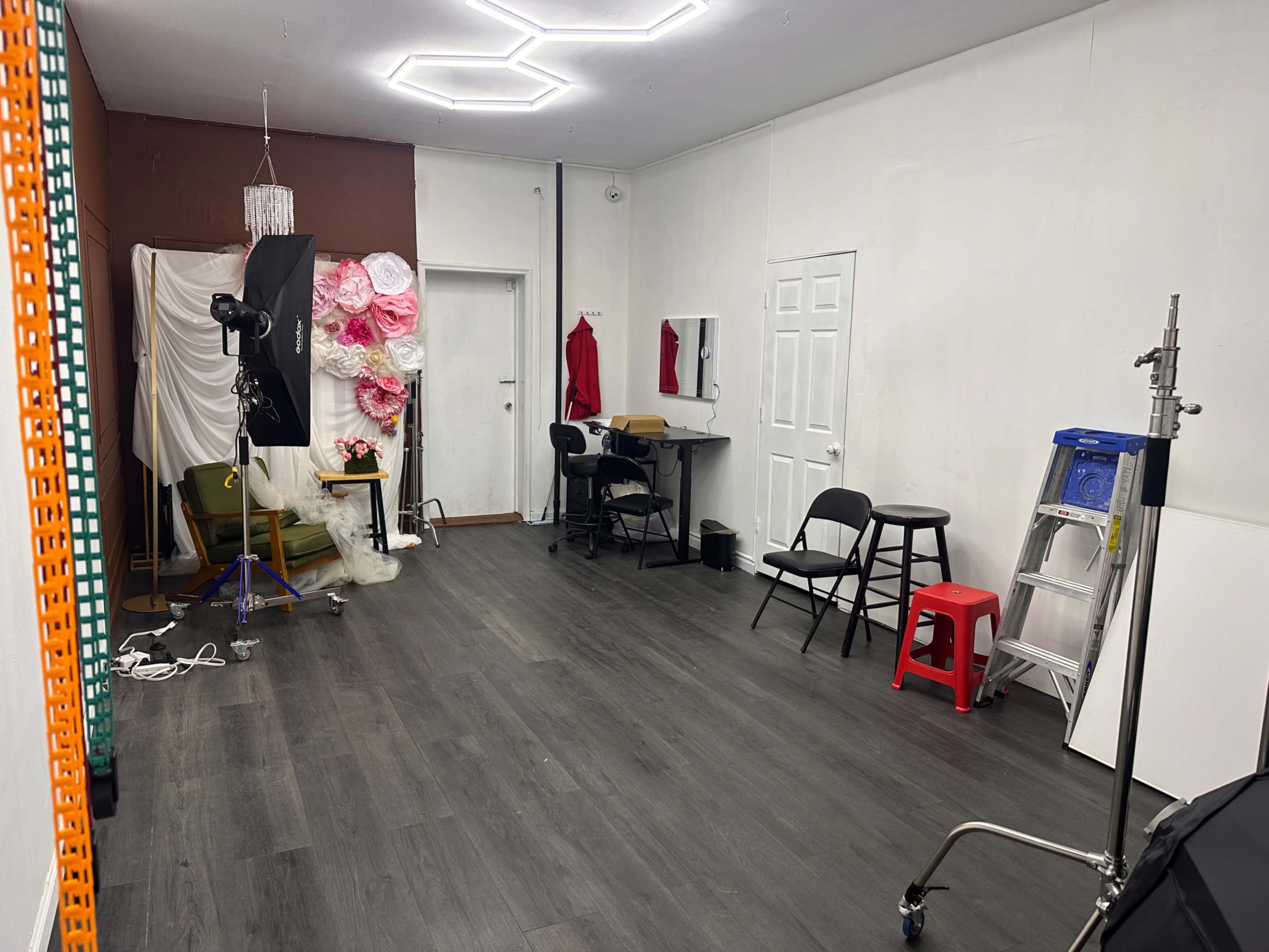 The image shows a photography studio with various equipment, including a light stand, chairs, and a backdrop decorated with flowers.