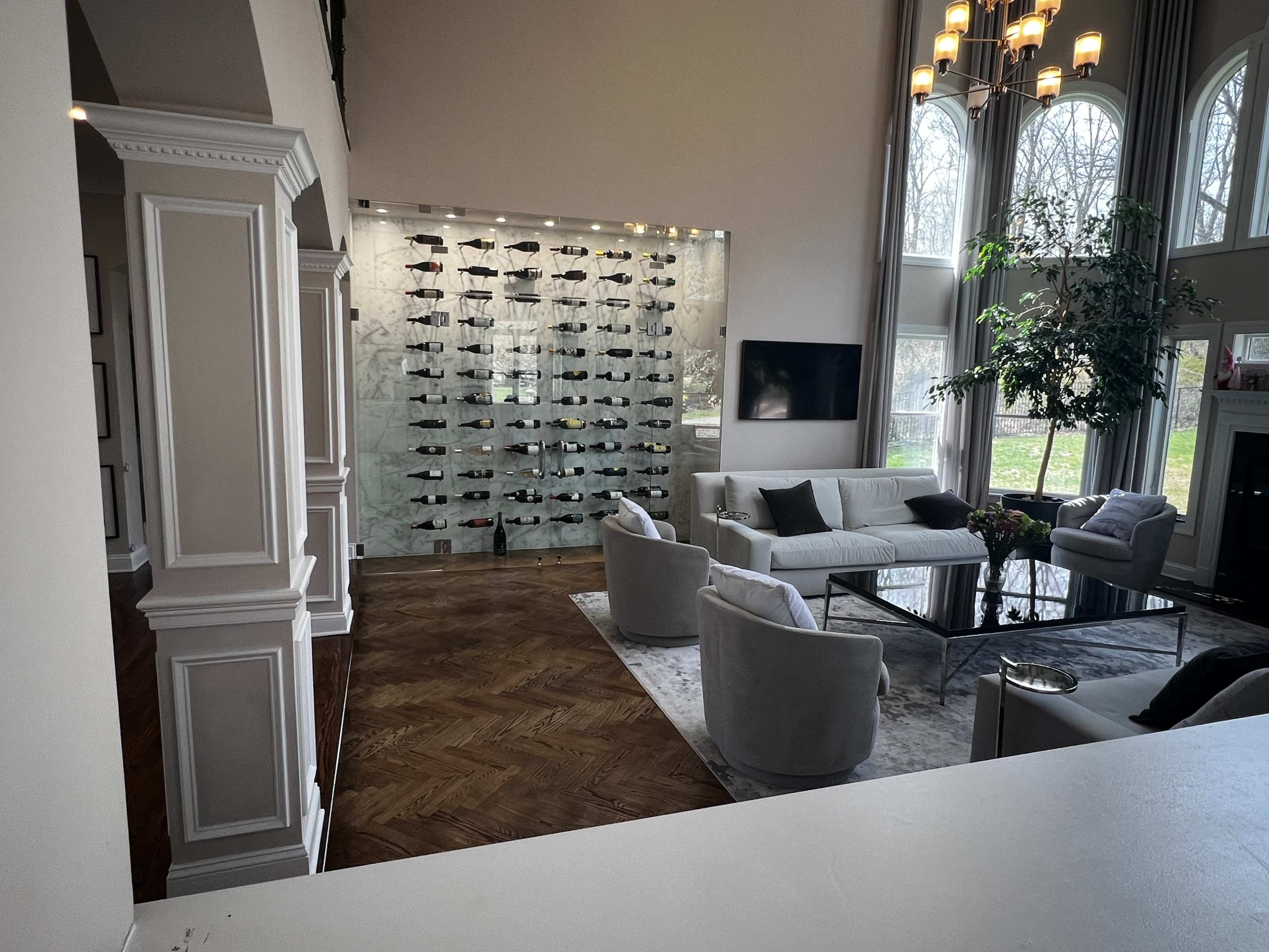A spacious living room with a modern wine display, comfortable seating, and large windows allowing natural light.