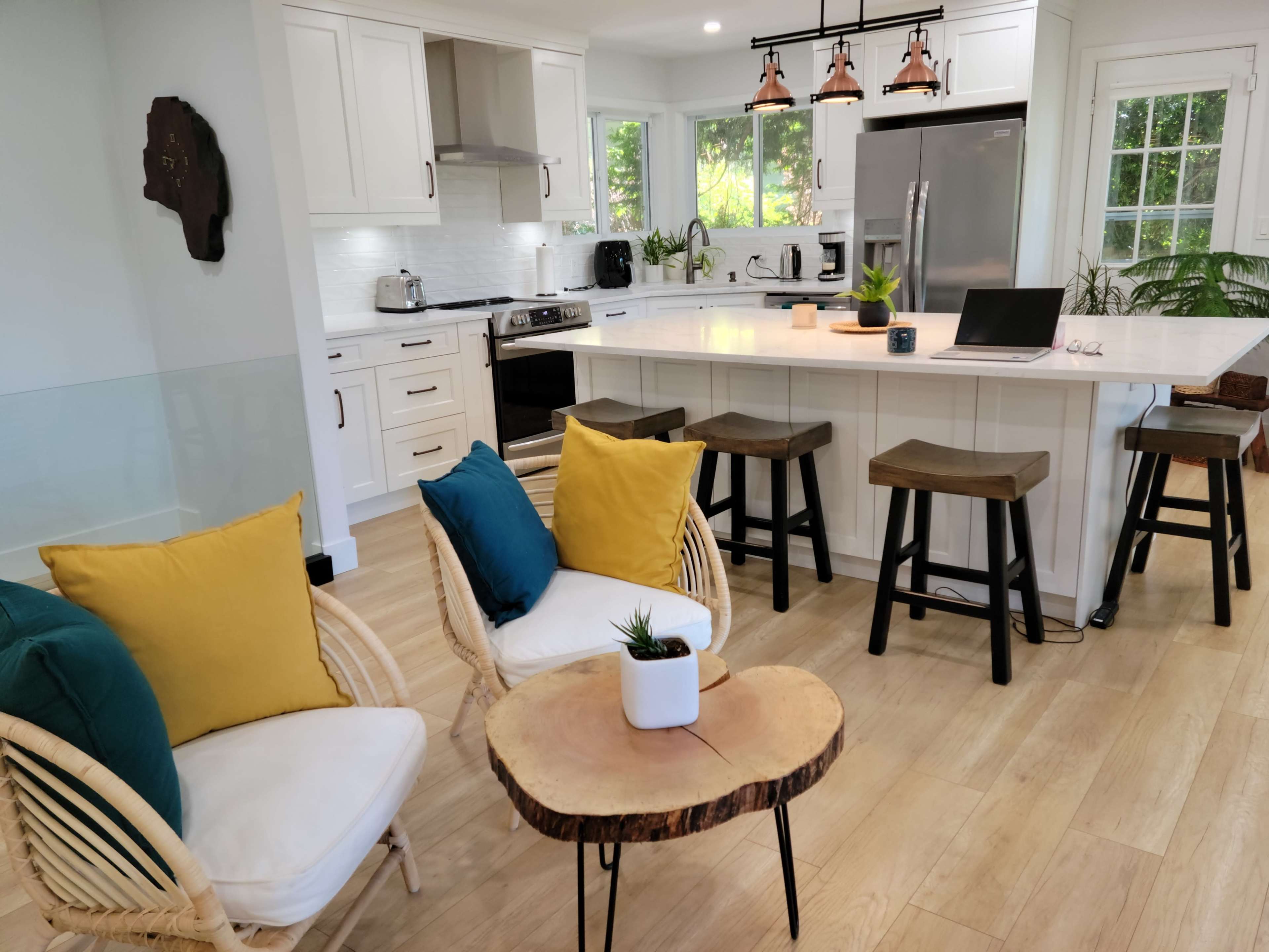 A modern kitchen with white cabinetry, a central island with bar stools, and a cozy seating area featuring two chairs and a small wooden coffee table.