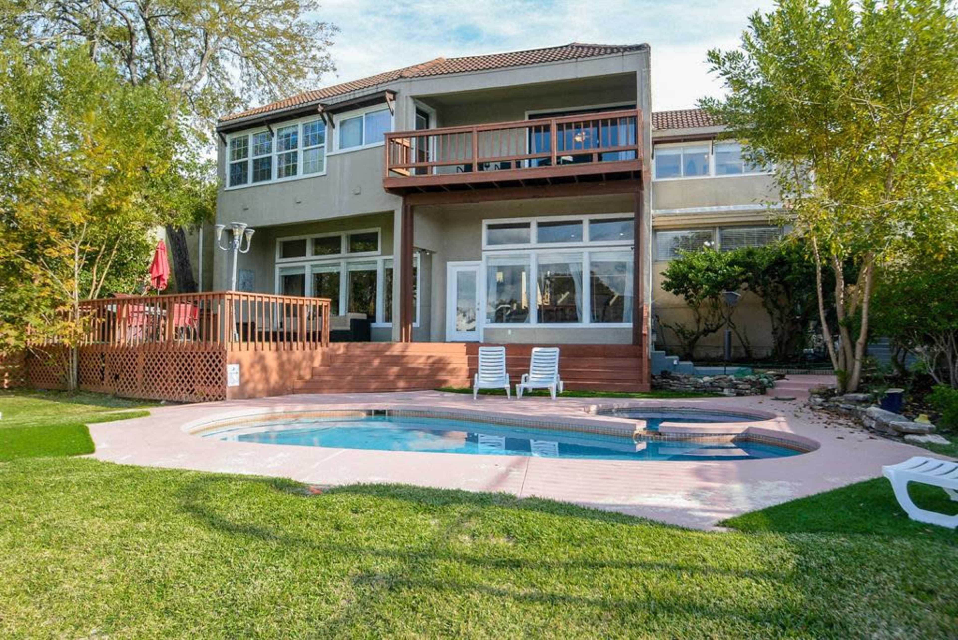 A two-story house with a deck overlooking a small pool, surrounded by a landscaped yard with trees and grass.