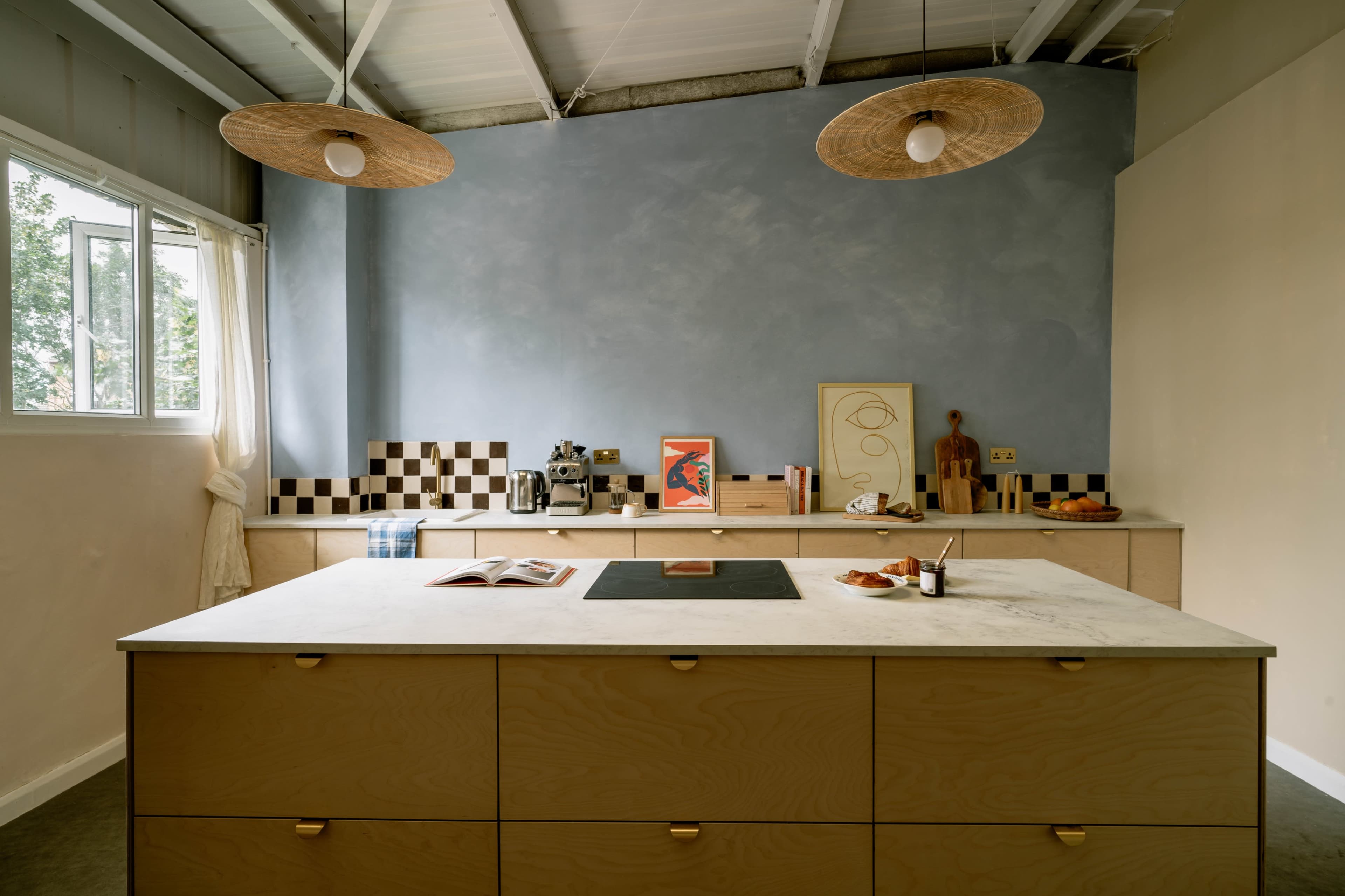 A modern kitchen featuring a central island with a marble countertop, wooden cabinetry, and a light blue wall adorned with decorative items.