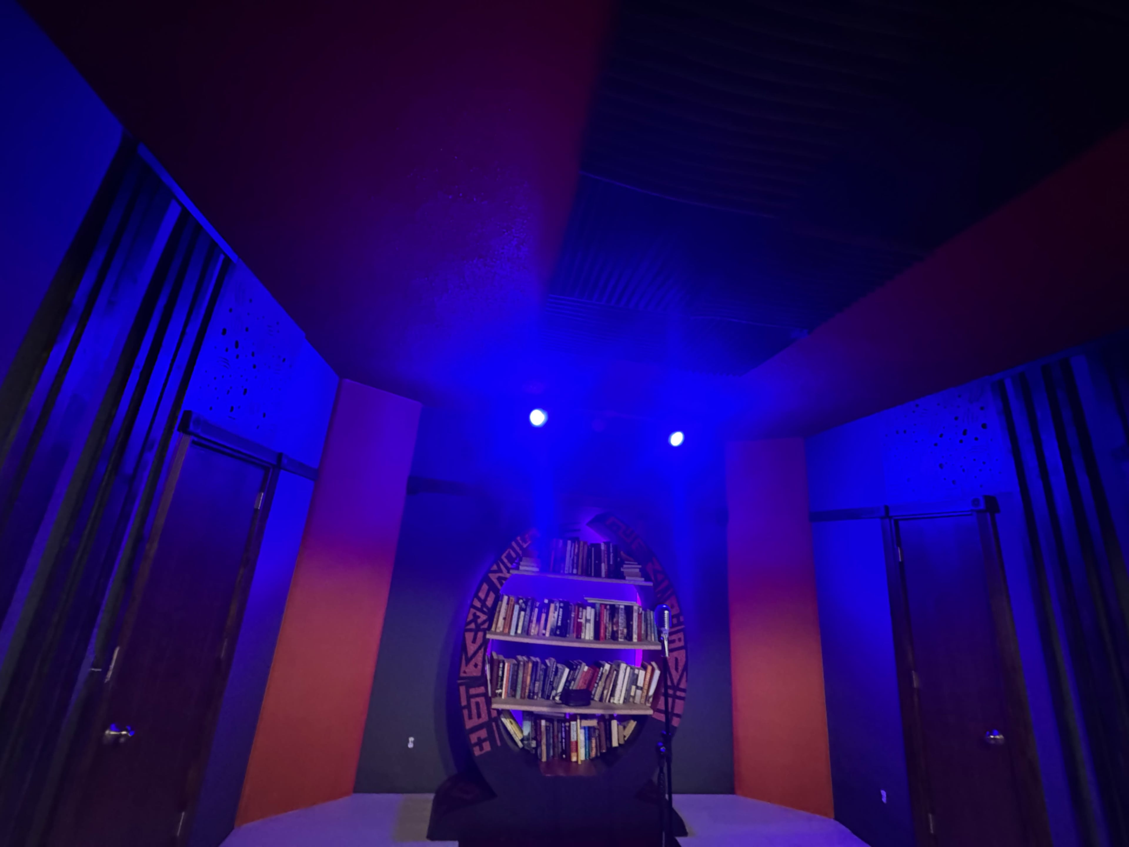 The image shows a dimly lit room with blue lighting, featuring a circular bookshelf filled with books at the center.
