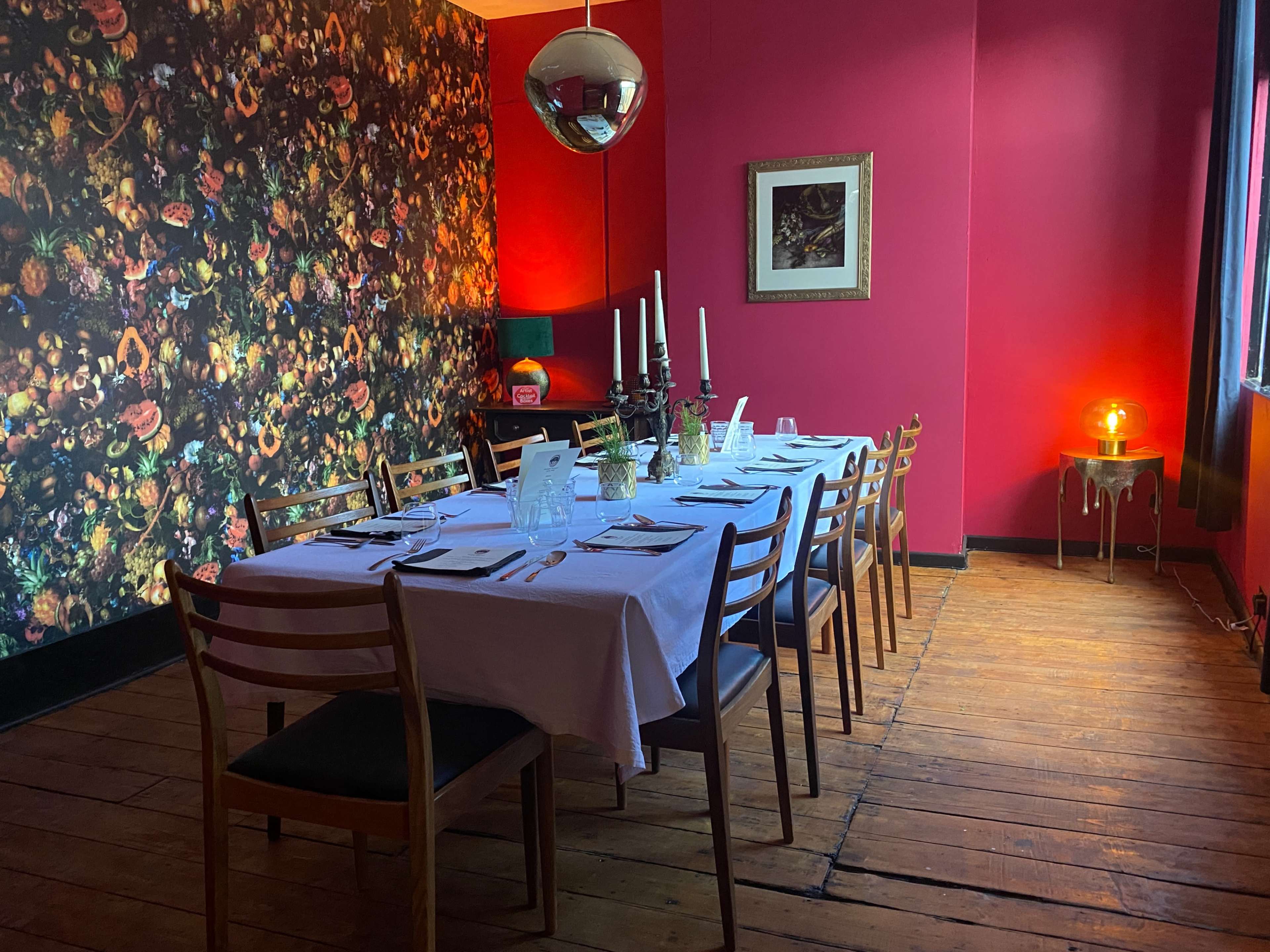 A long dining table is set for a meal in a brightly colored room with floral wallpaper and a large disco ball.