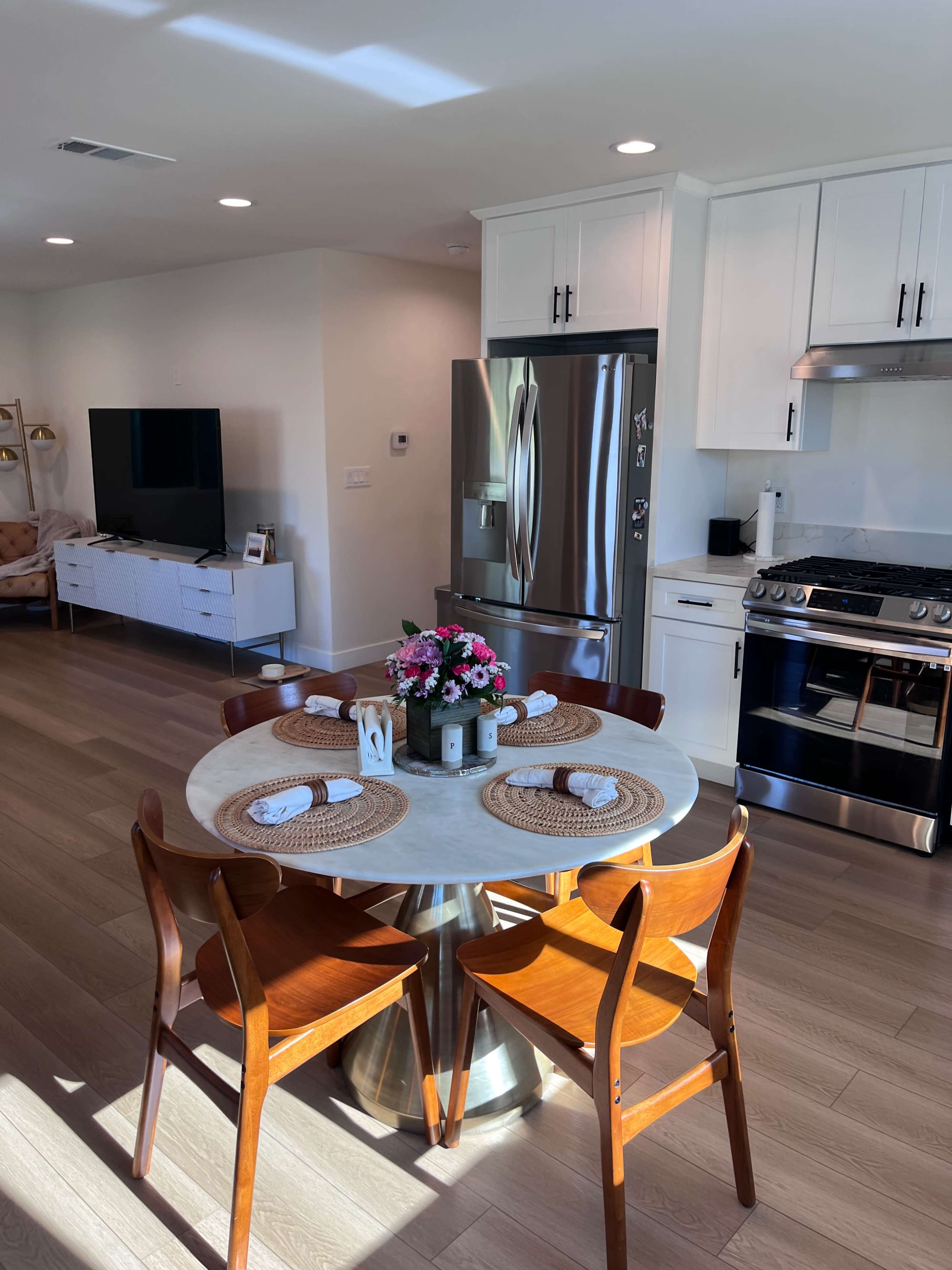 A modern kitchen features a round dining table set with placemats, four wooden chairs, and stainless steel appliances.