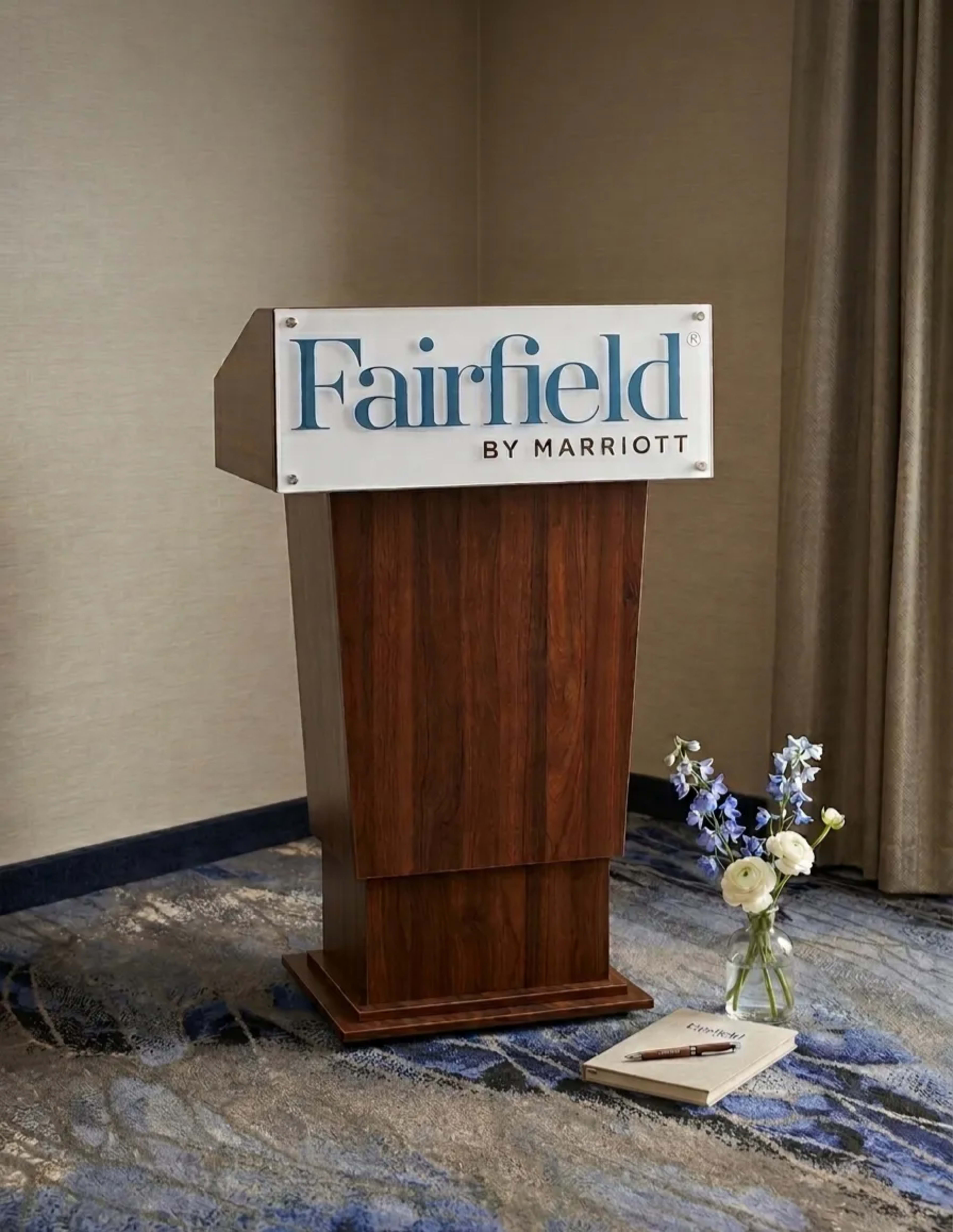 A wooden podium with a sign reading "Fairfield by Marriott" stands next to a bouquet of flowers on a patterned carpet.