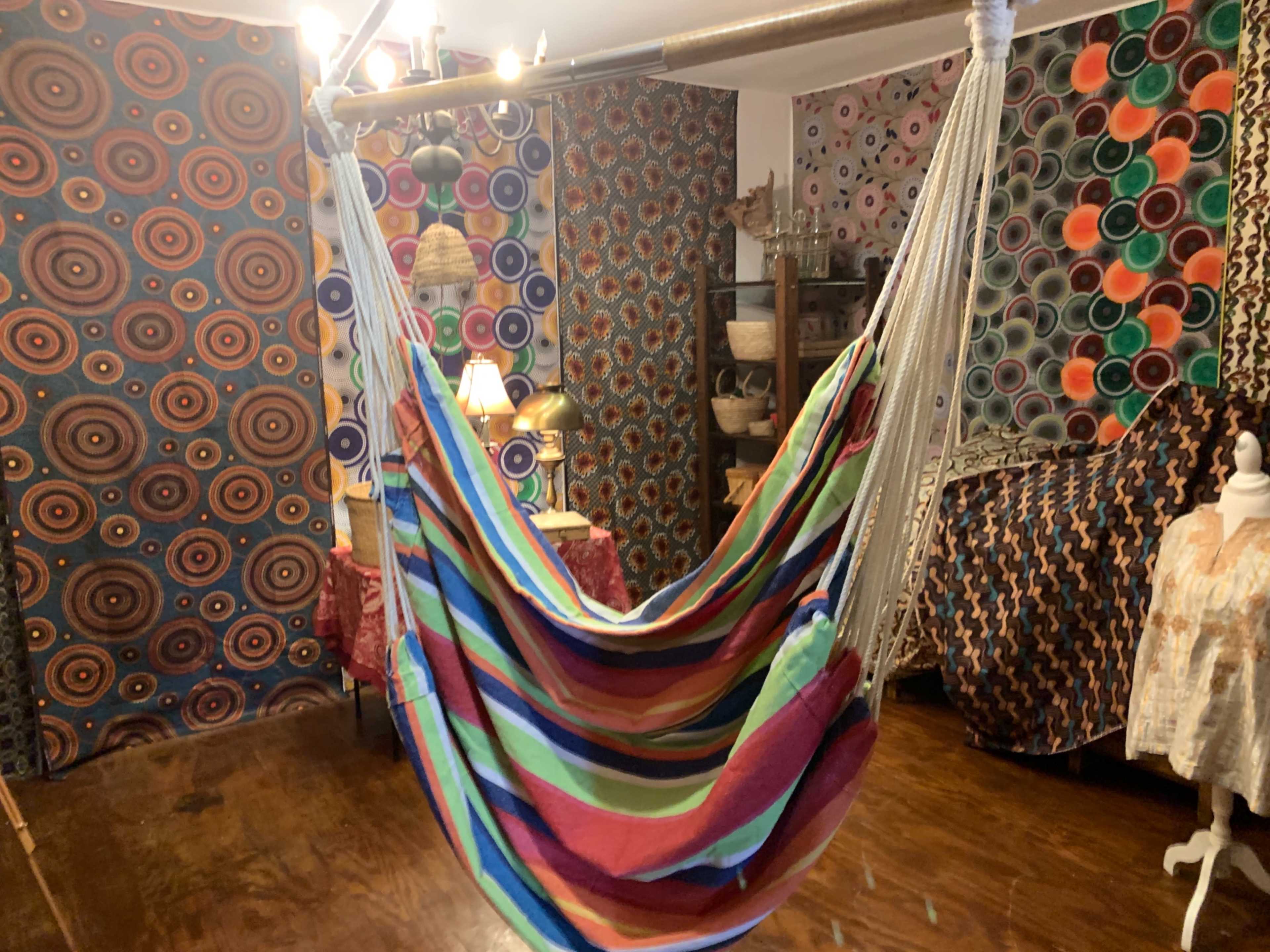 A colorful hammock hangs in a room decorated with patterned wallpapers and eclectic furnishings.