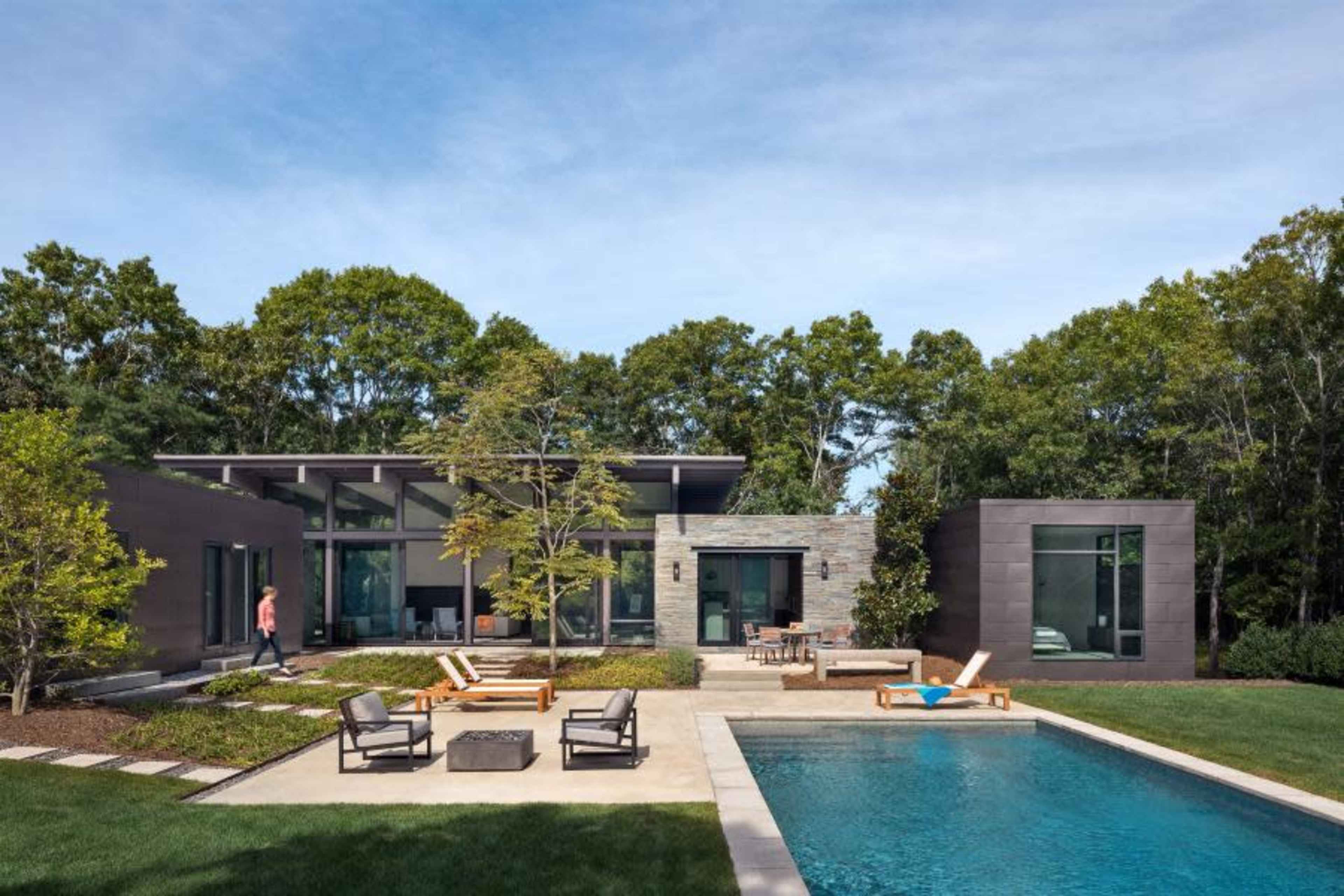 A modern house with a flat roof, large windows, and a pool is surrounded by landscaped greenery and outdoor seating areas.