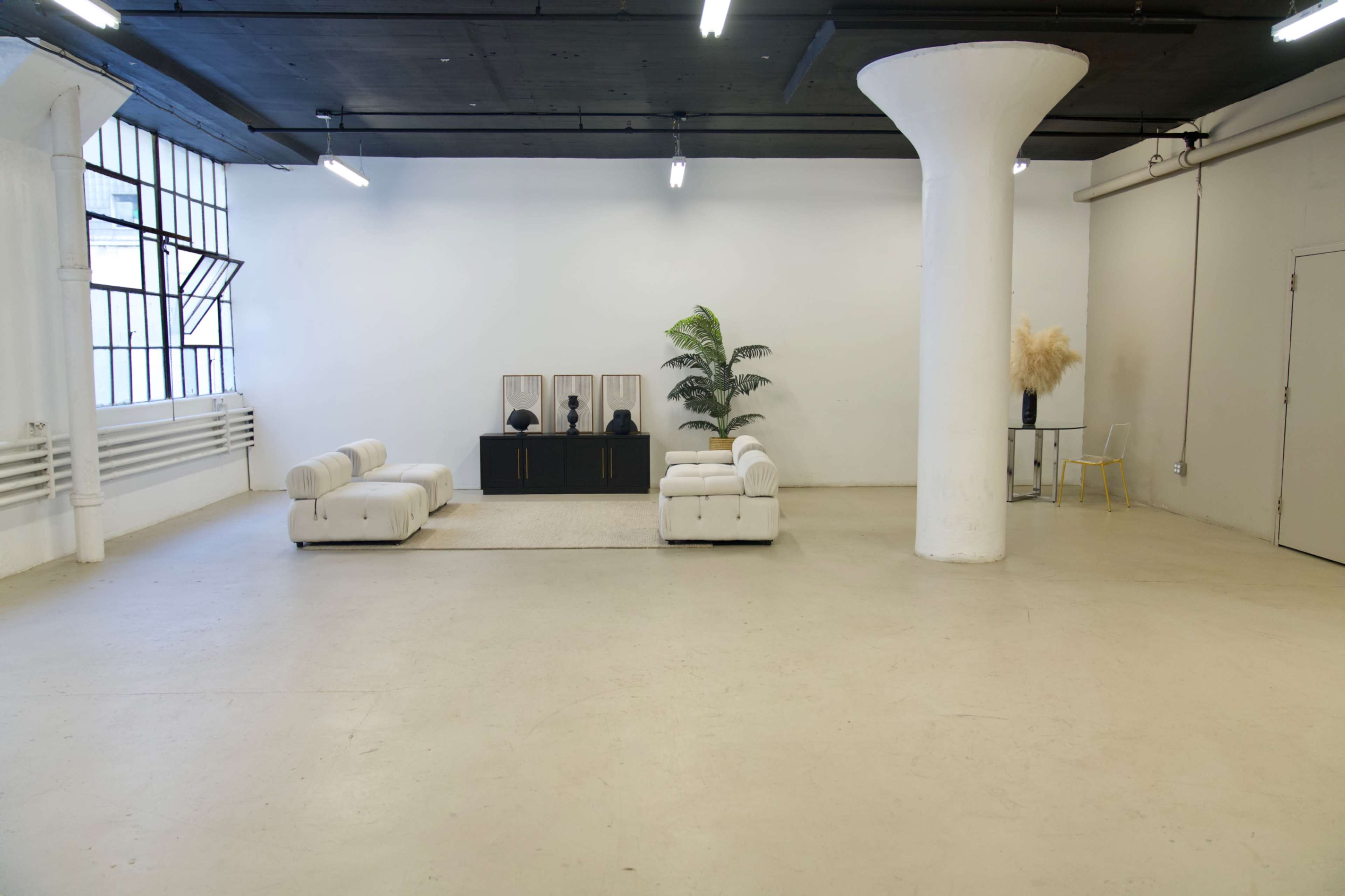 A spacious, minimalistic room with two white sofas, a black cabinet with mirrors, a potted plant, and a decorative arrangement on the floor.