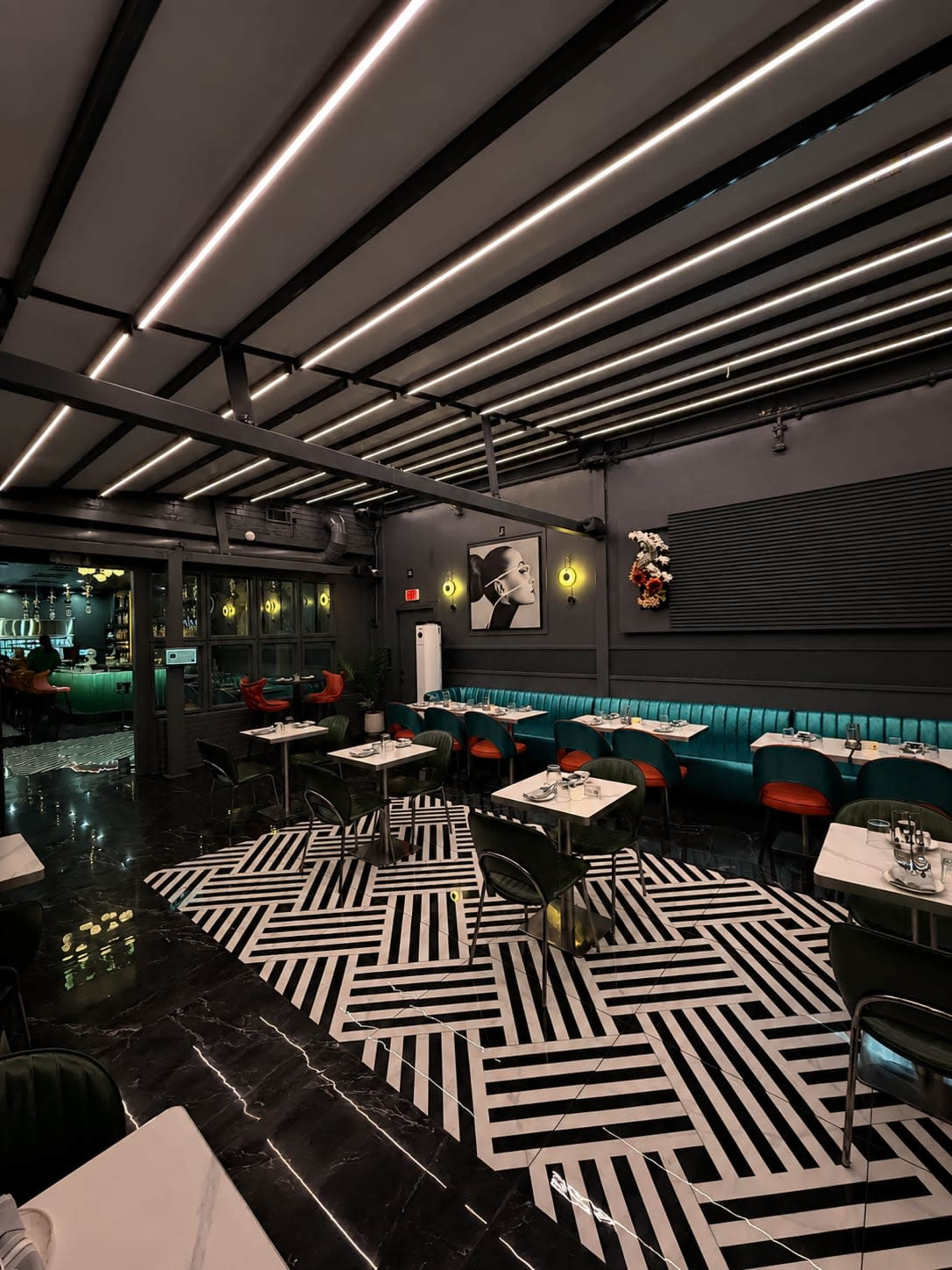 The interior of a modern restaurant features a geometric black and white patterned floor, teal seating, and linear lighting on the ceiling.