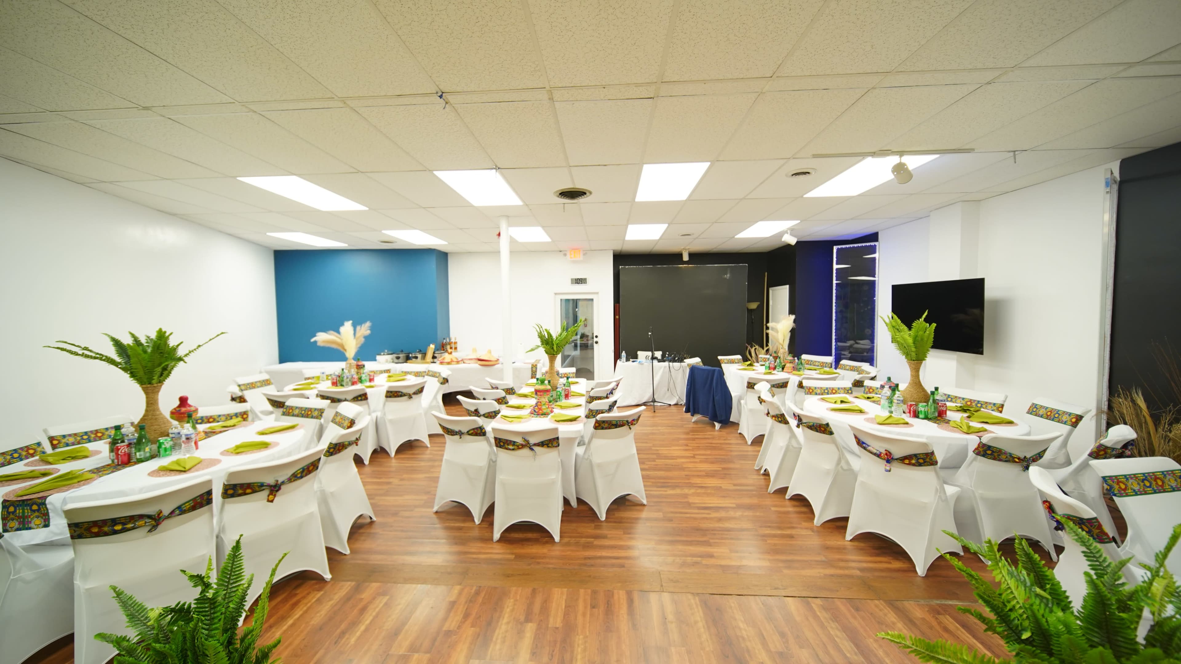 The image shows a banquet hall arranged with round tables covered in white tablecloths, decorated with centerpieces and seating for guests.