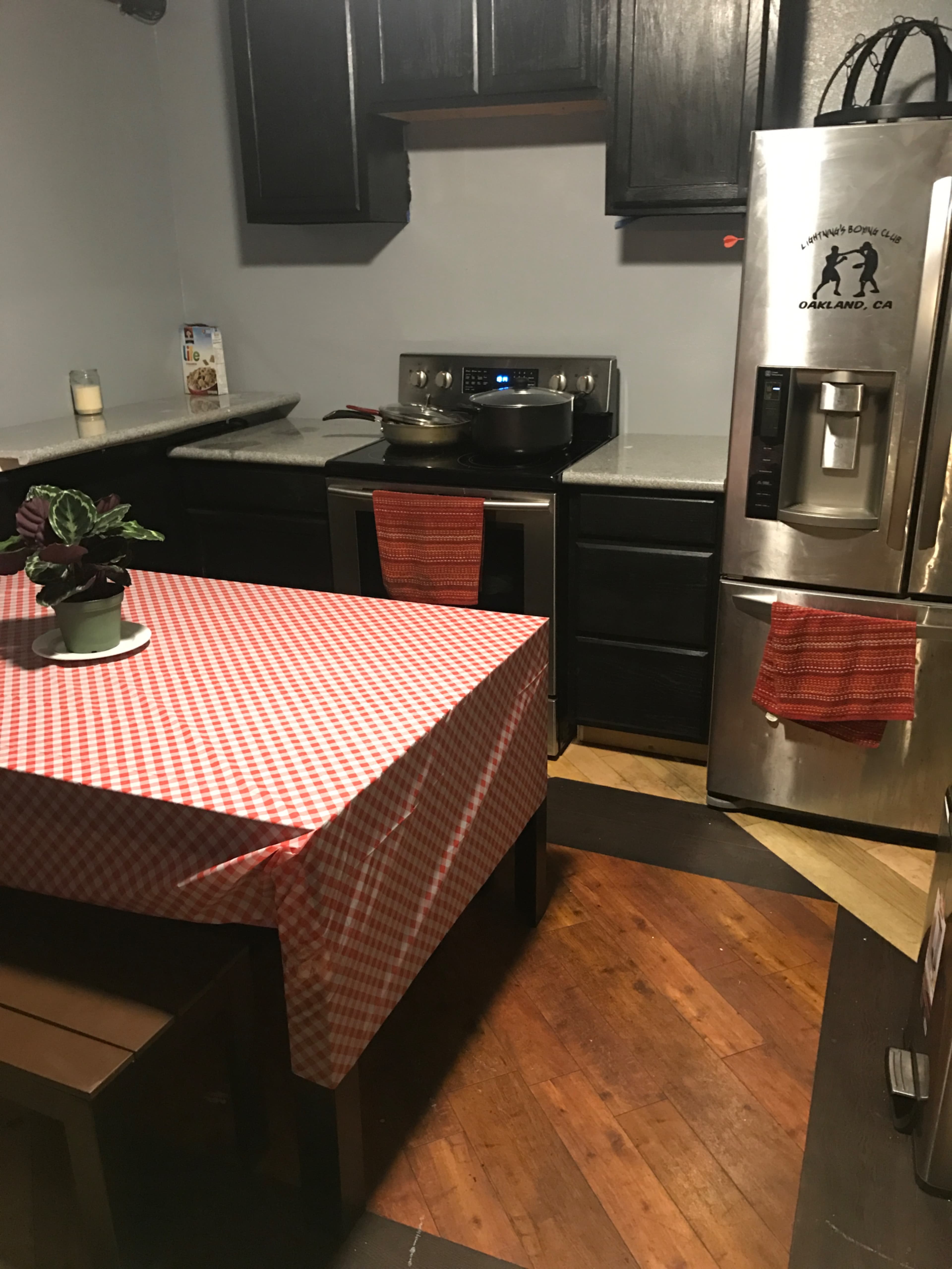 A small kitchen with a checkered tablecloth covering a table, stainless steel appliances, and dark wooden cabinets.