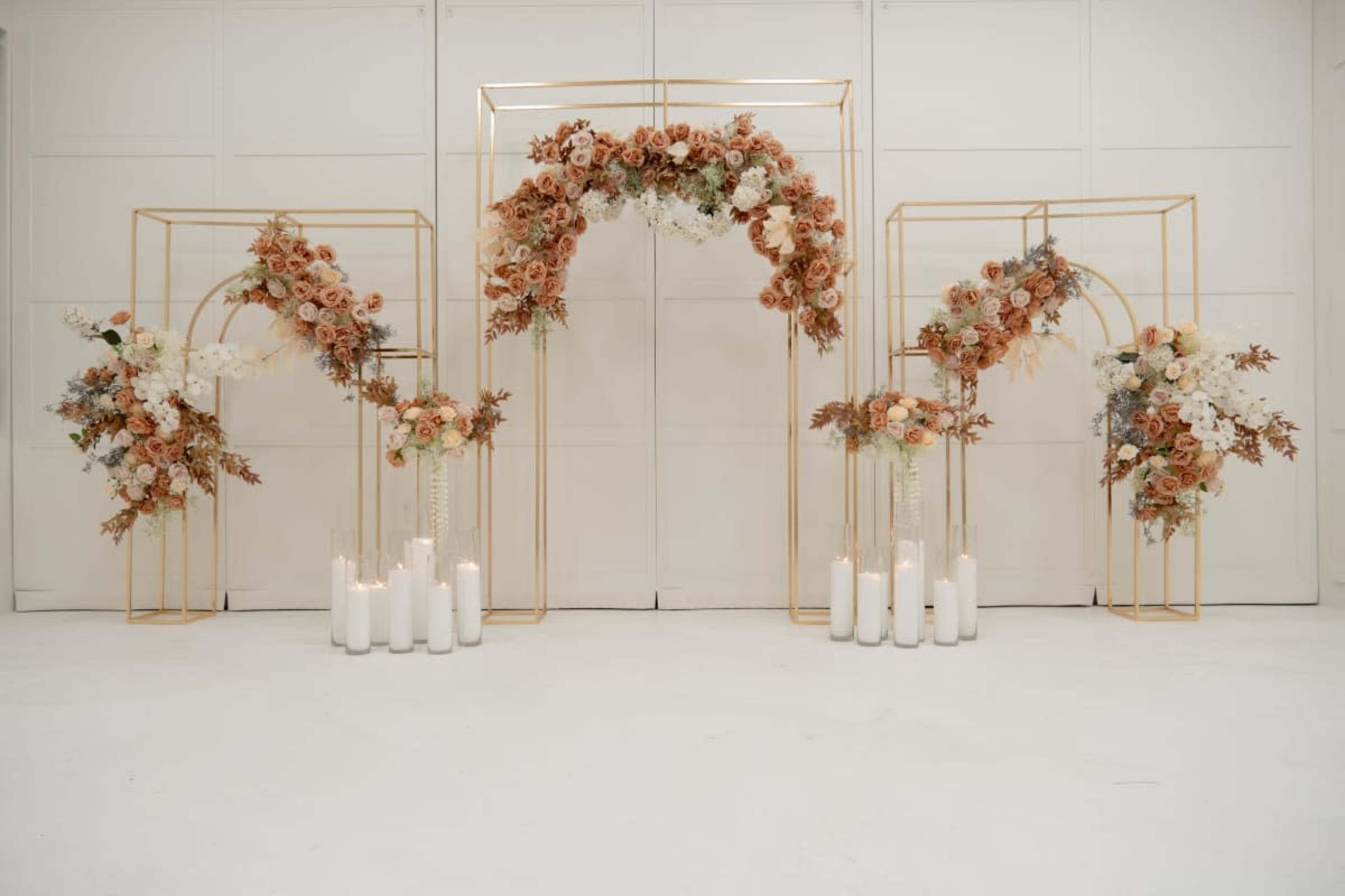 The image features a decorative display with golden arches adorned with flowers and several white candles arranged on the ground.