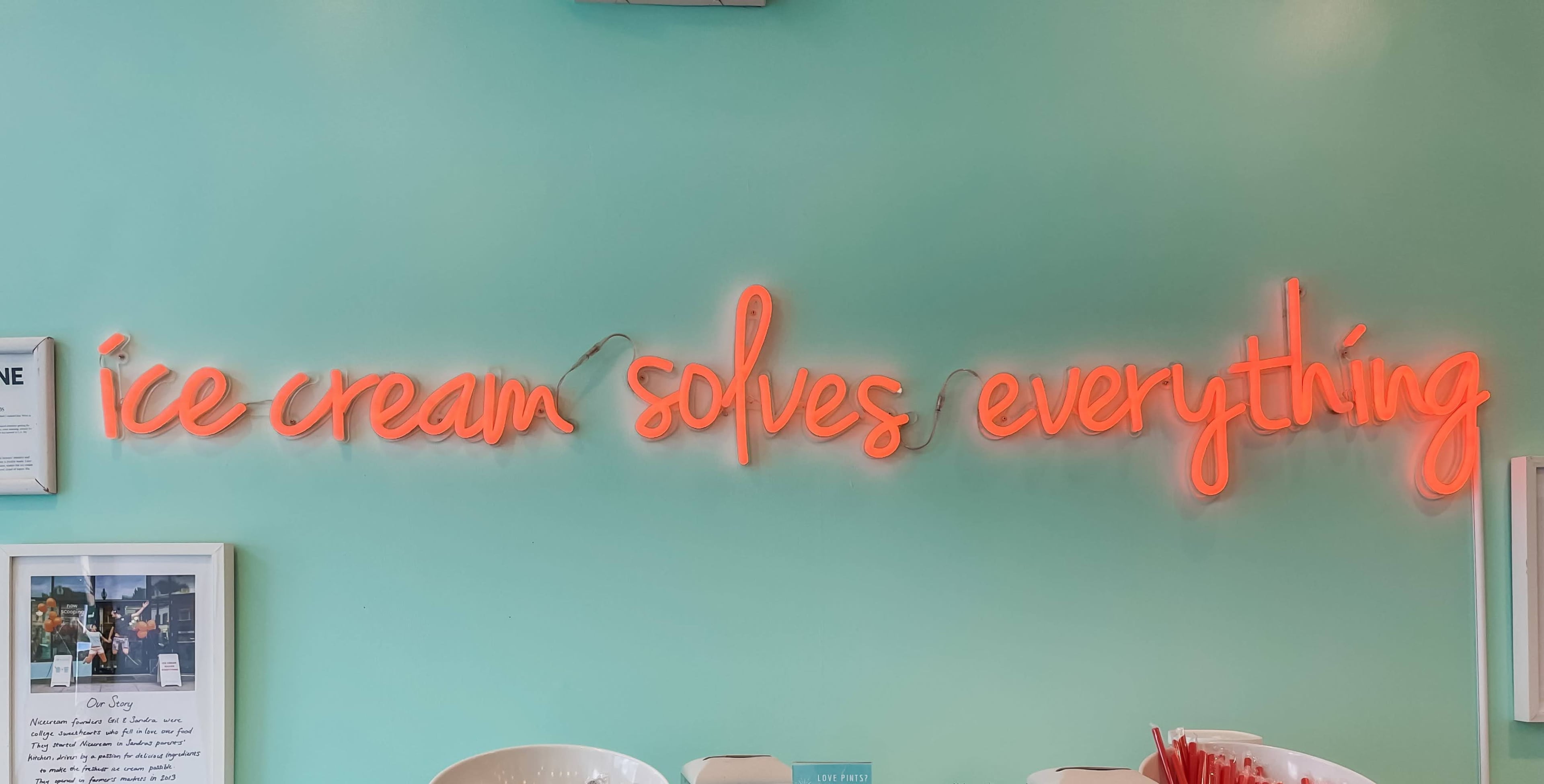 A neon sign that reads "ice cream solves everything" is illuminated on a turquoise wall.